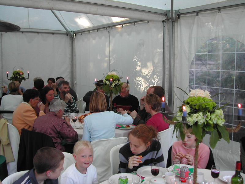 People gathered around tables in a decorated tent, eating, drinking, and socializing during a communion celebration.