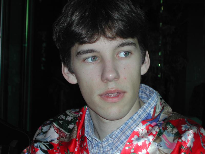 A young man in a colorful floral robe looks to the side with a neutral expression.