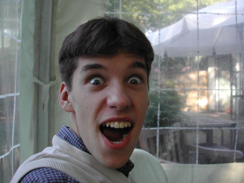 A young man with short brown hair smiles widely with an excited expression, looking at the camera.