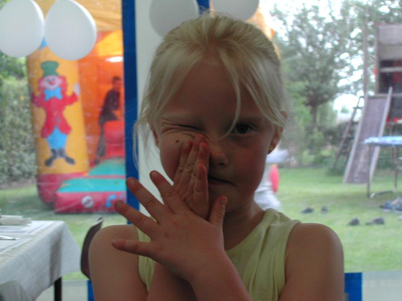 A young girl playfully covers one eye with her hand at a communion party.