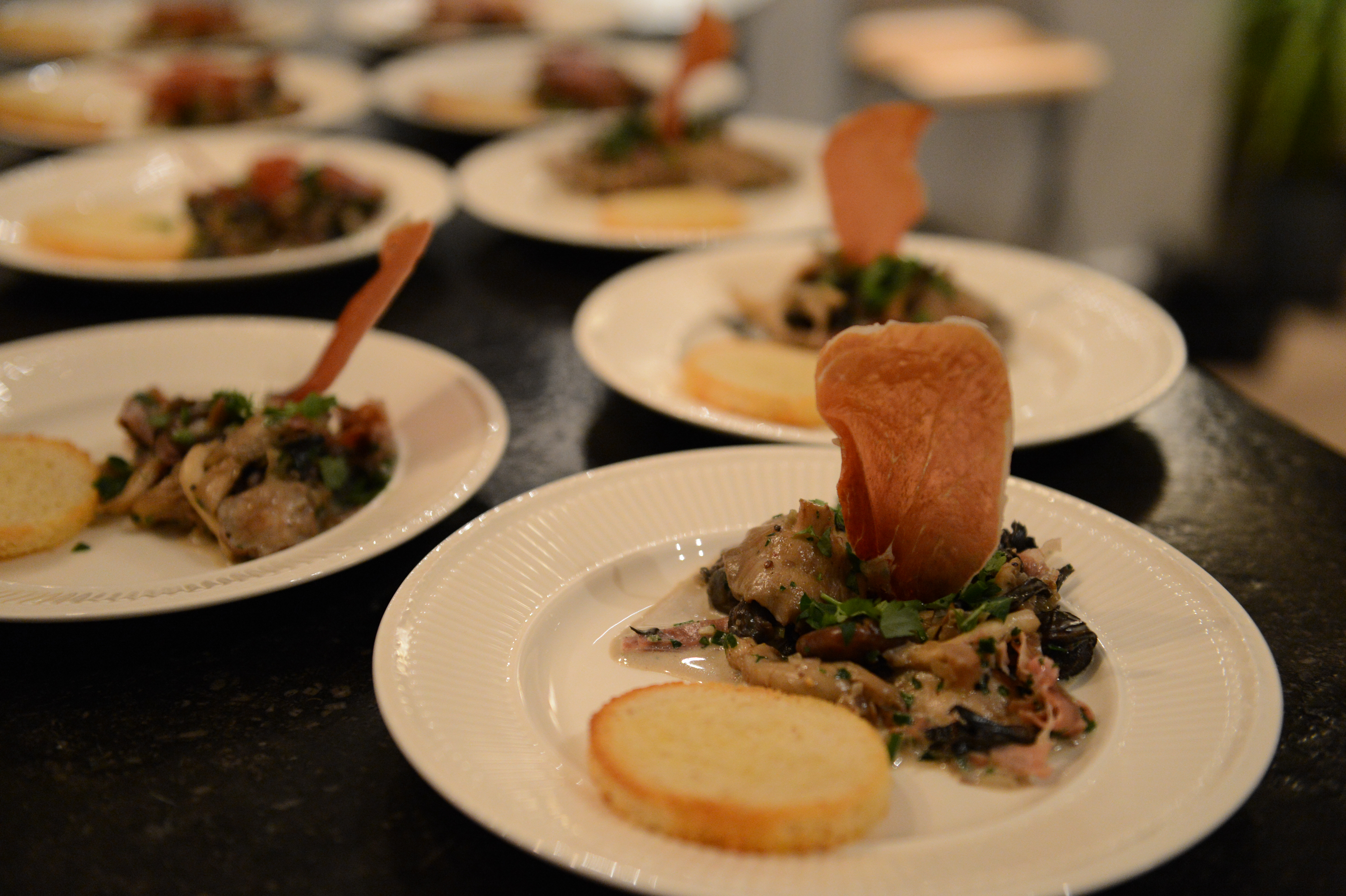 Plates of prepared food with bread and garnishes are arranged on a table during a cooking class.