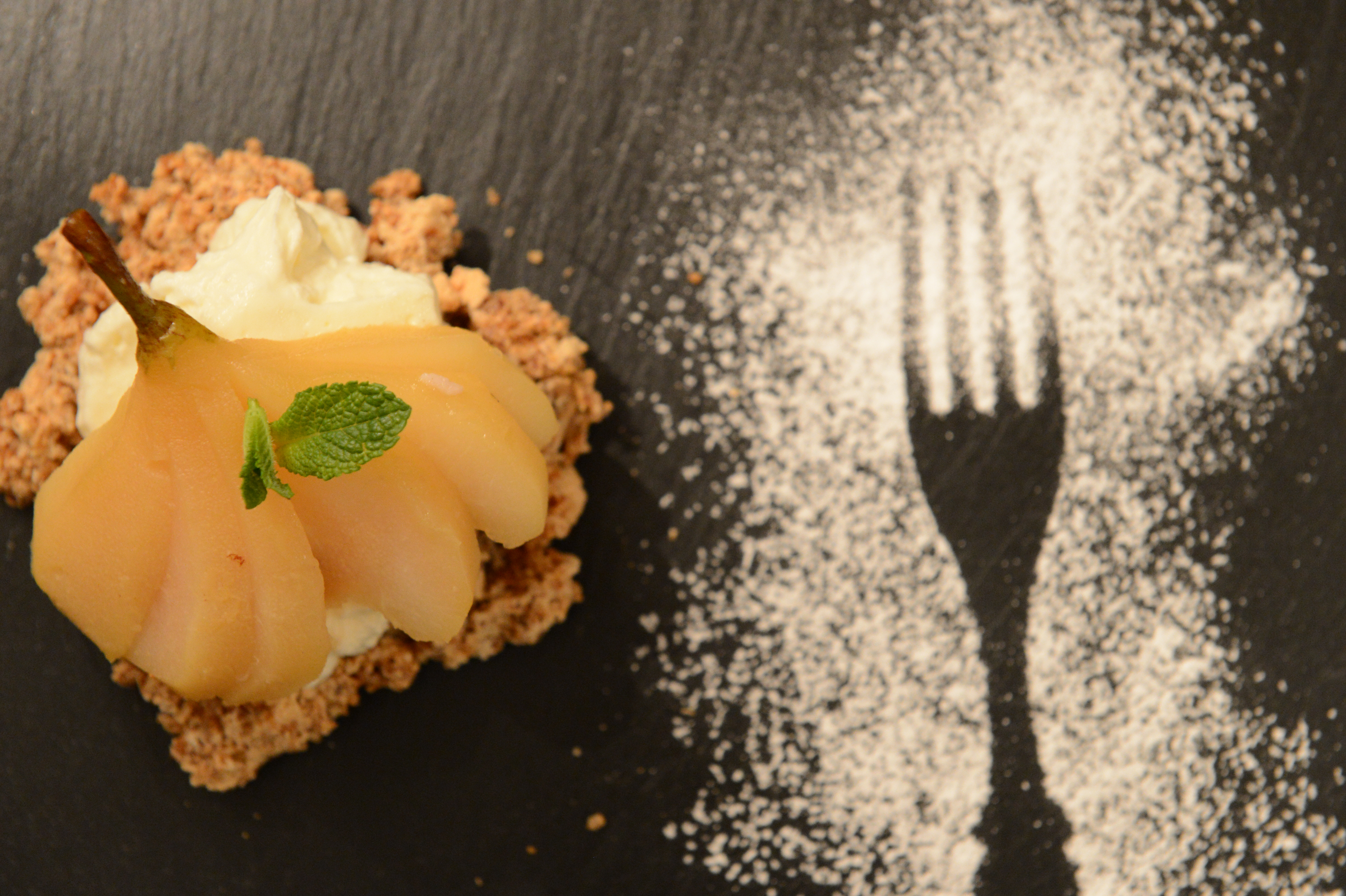 A plated dessert with poached pear, cream, and crumble, next to a fork silhouette made with powdered sugar.