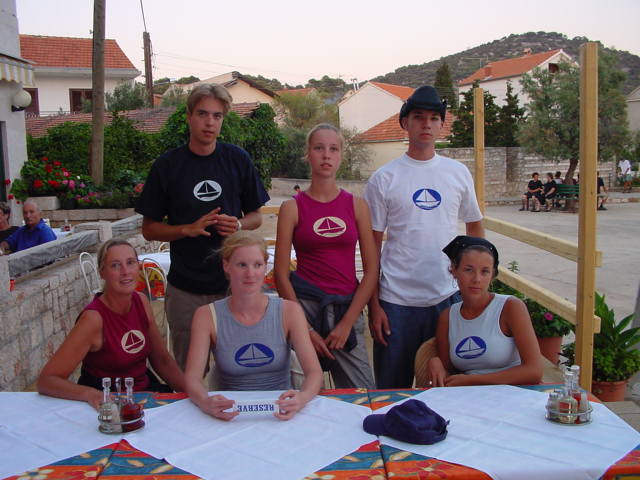 Six people wearing matching shirts pose at an outdoor restaurant table with a "Reserved" sign.