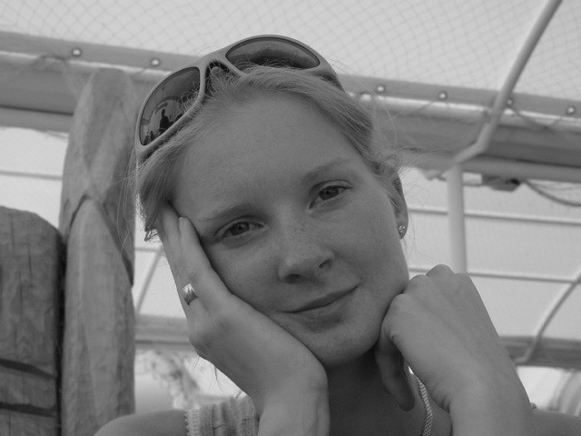 A woman with sunglasses on her head rests her face on her hand and looks at the camera.