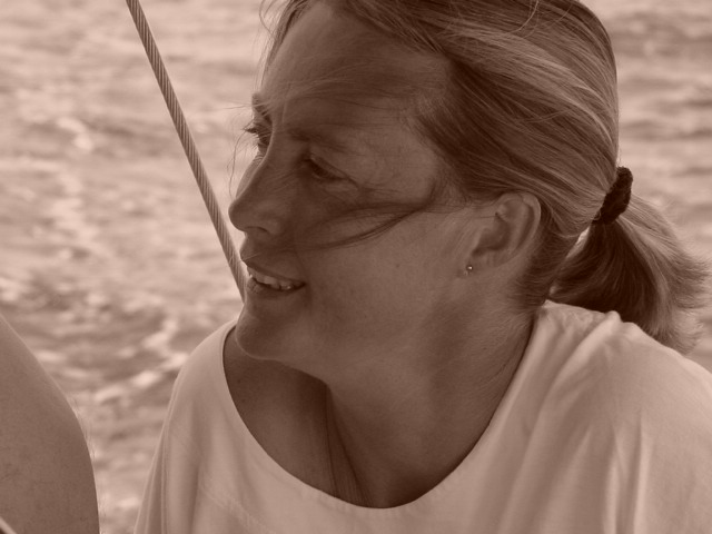 A woman with tied-back hair smiles while looking to the side on a boat with water in the background.