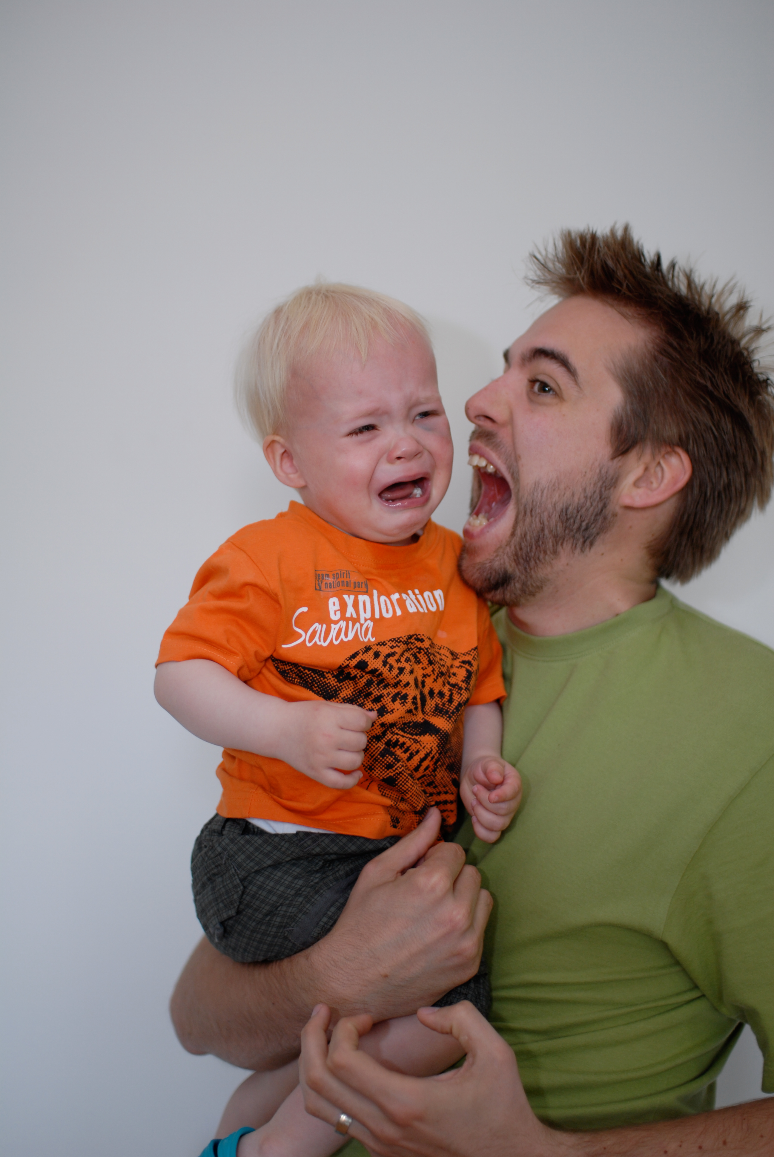 A man holds a crying toddler in his arms, looking at him with an open mouth.