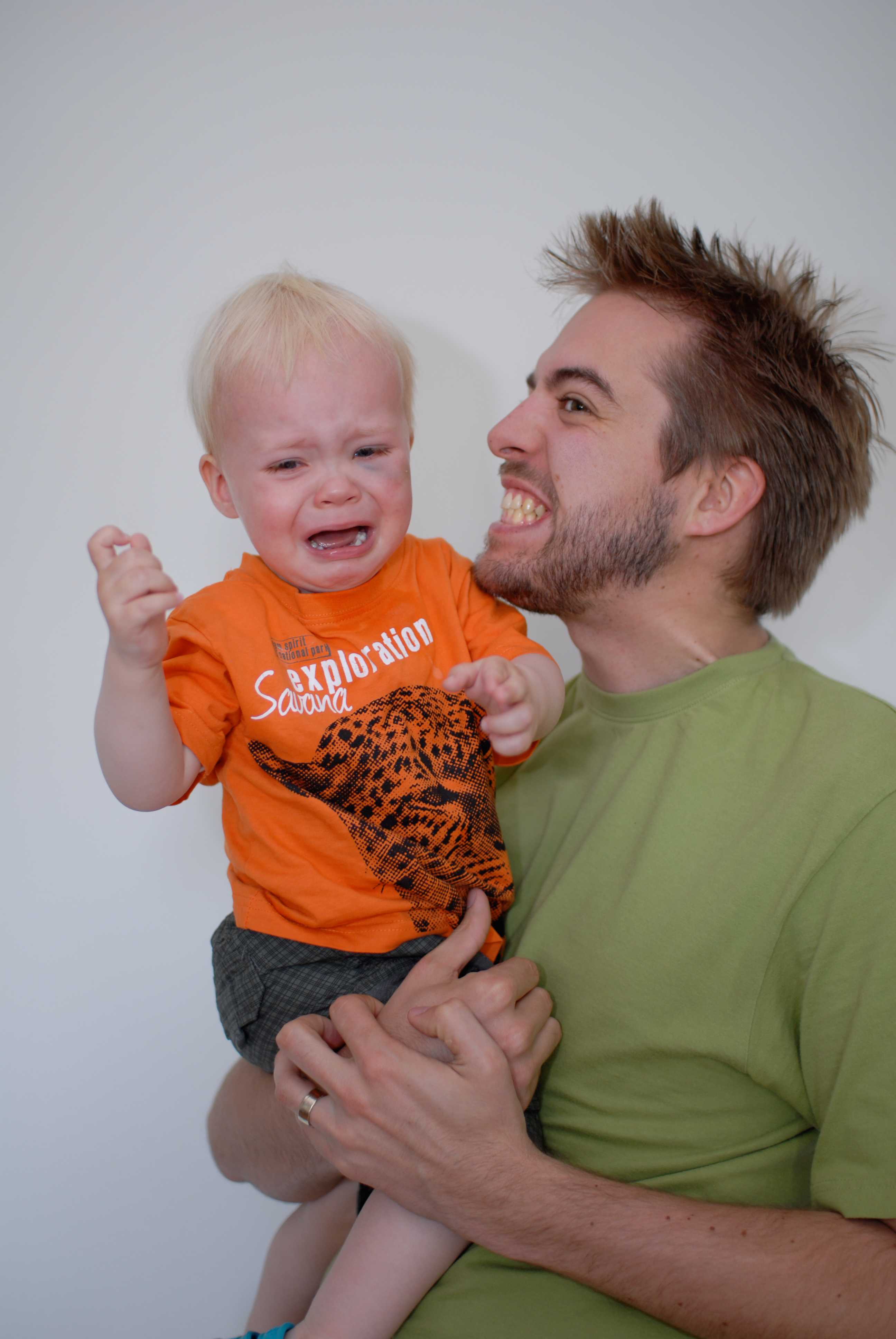 A man in a green shirt holds a crying toddler in an orange shirt after a fall.