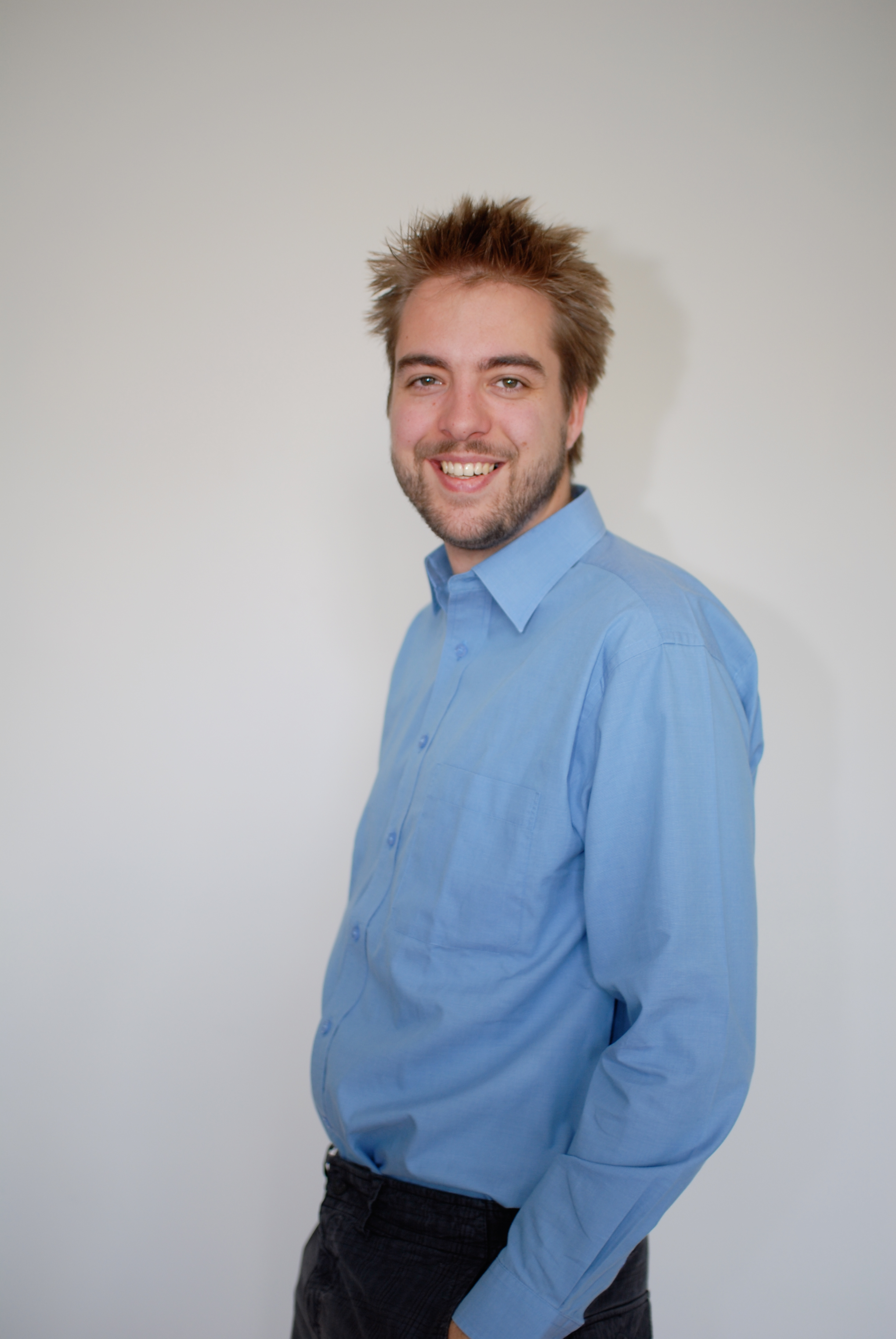 A man wearing a blue shirt smiles at the camera against a plain white background.