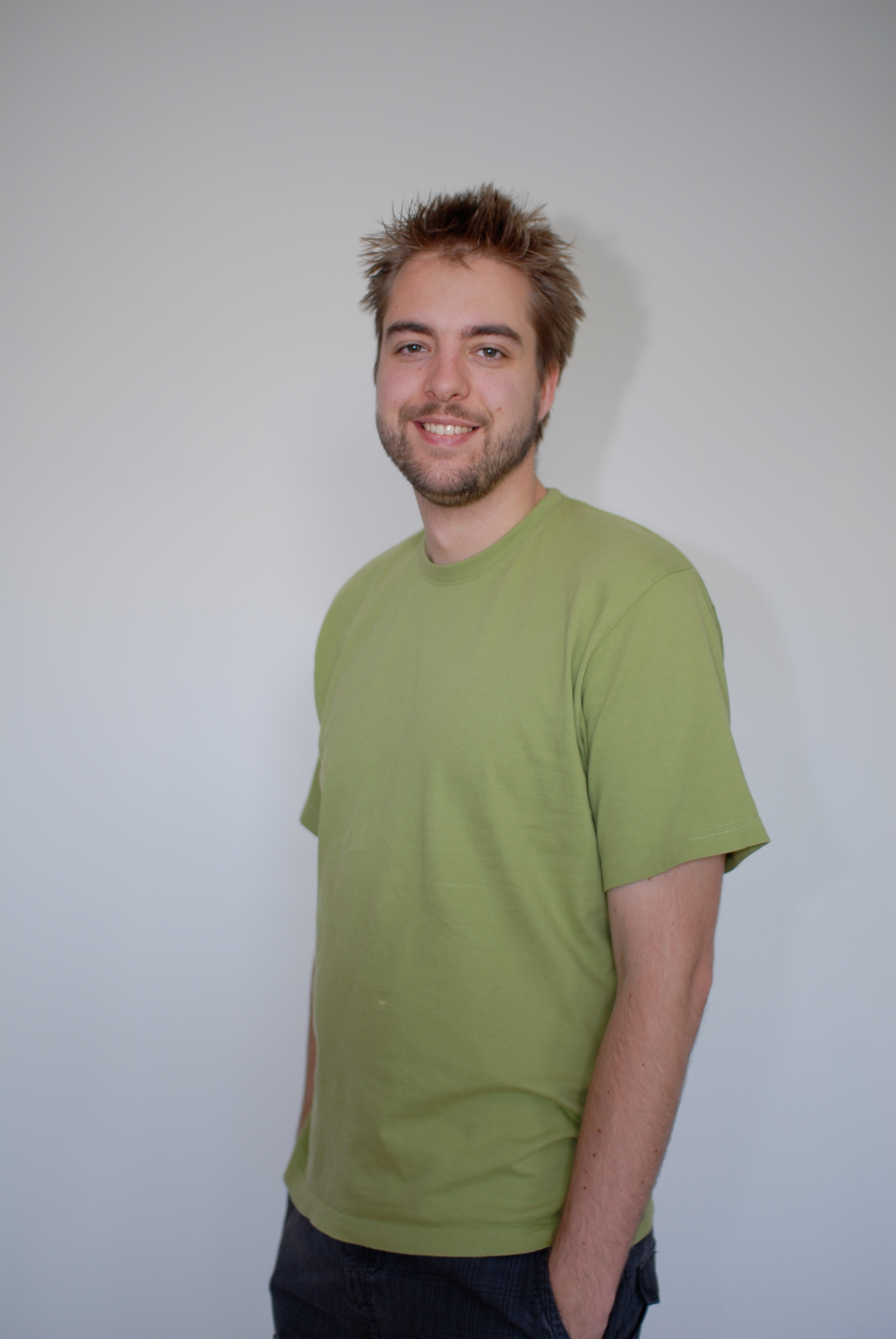 A man with short, spiky hair and a beard smiles while wearing a green T-shirt against a plain background.