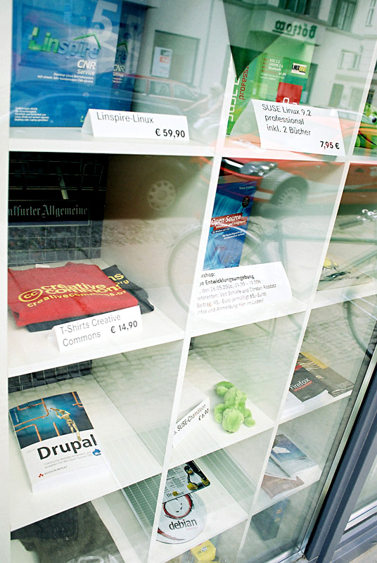A bookstore window display featuring a Drupal book, Linux software, Creative Commons T-shirts, and other tech-related items.