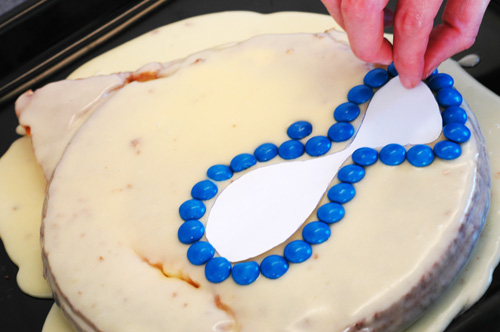 A hand decorating a cake with blue m&amp;m's