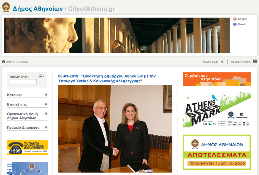 A man and a woman shake hands and smile in an office setting with wooden bookshelves in the background.