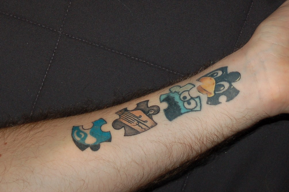 A tattoo on a forearm features four puzzle pieces with different logos, including the Drupal Druplicon symbol.