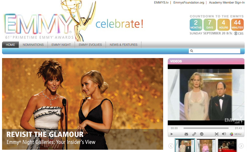 Two presenters stand on stage at the Emmy Awards, smiling and speaking into a microphone.