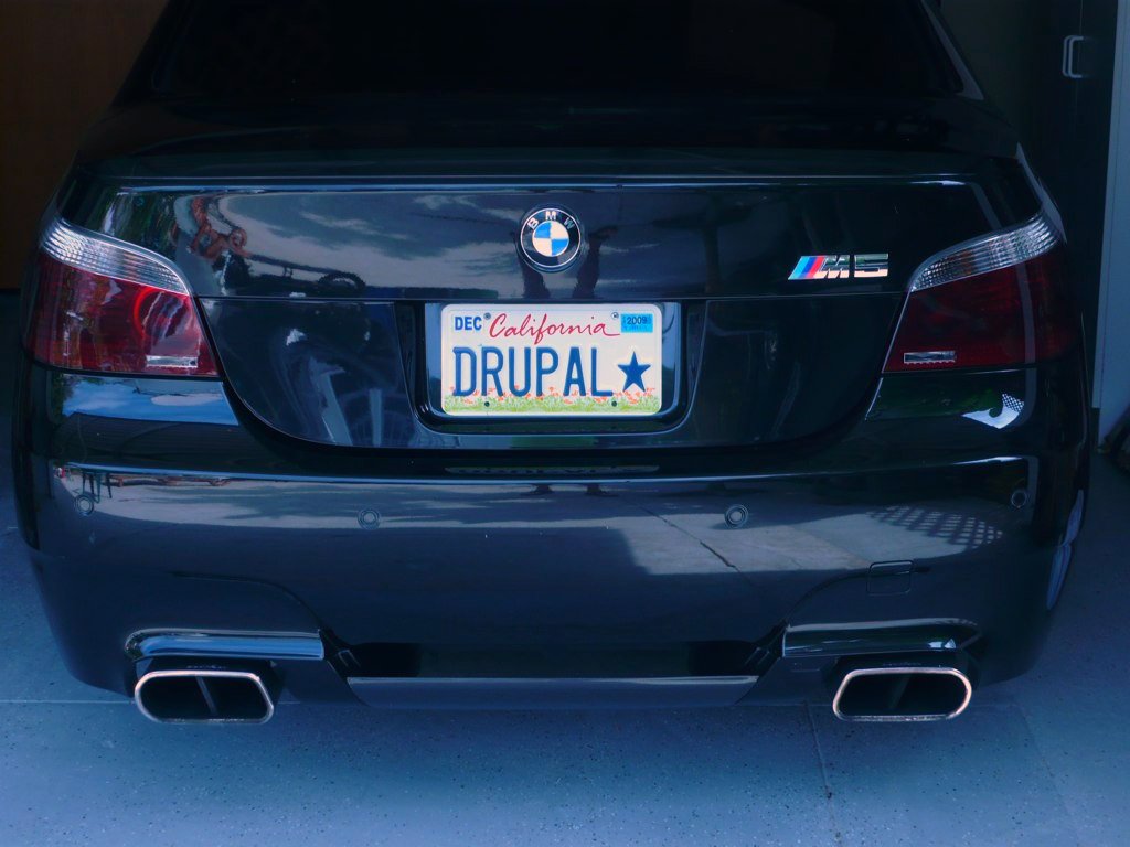 A black BMW M5 with a custom California license plate that reads "DRUPAL", parked in a garage.