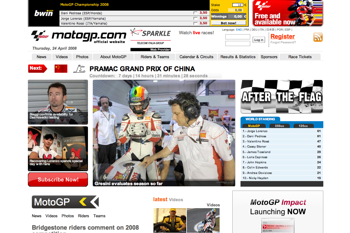 A MotoGP rider in full gear listens to a team member wearing a headset in the pit area.