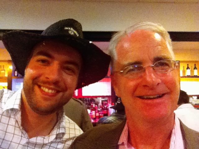 Two smiling men pose for a photo in a bar, one wearing a black hat.