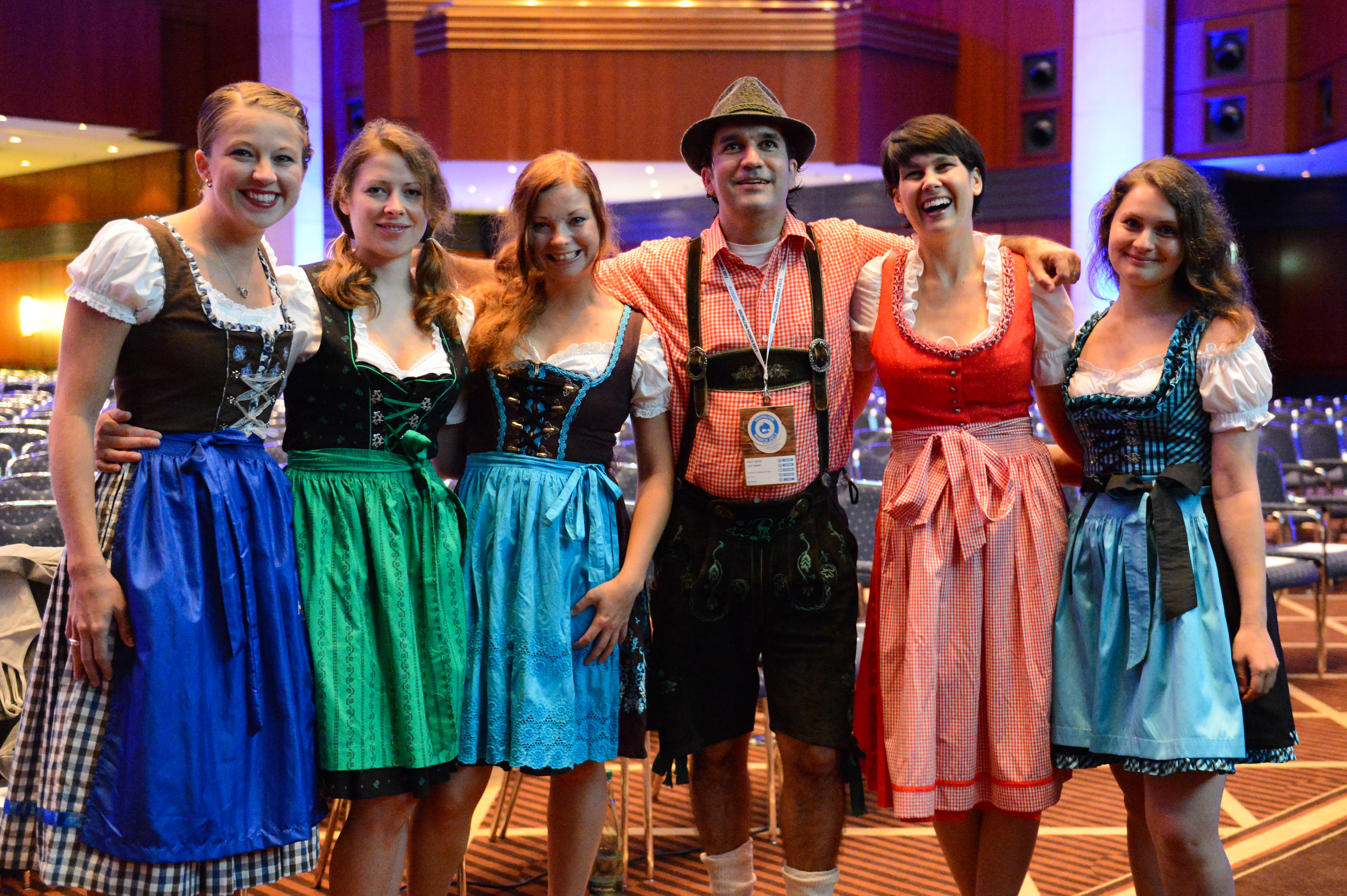 A group of six people in traditional Bavarian clothing pose together and smile at the camera during the event.