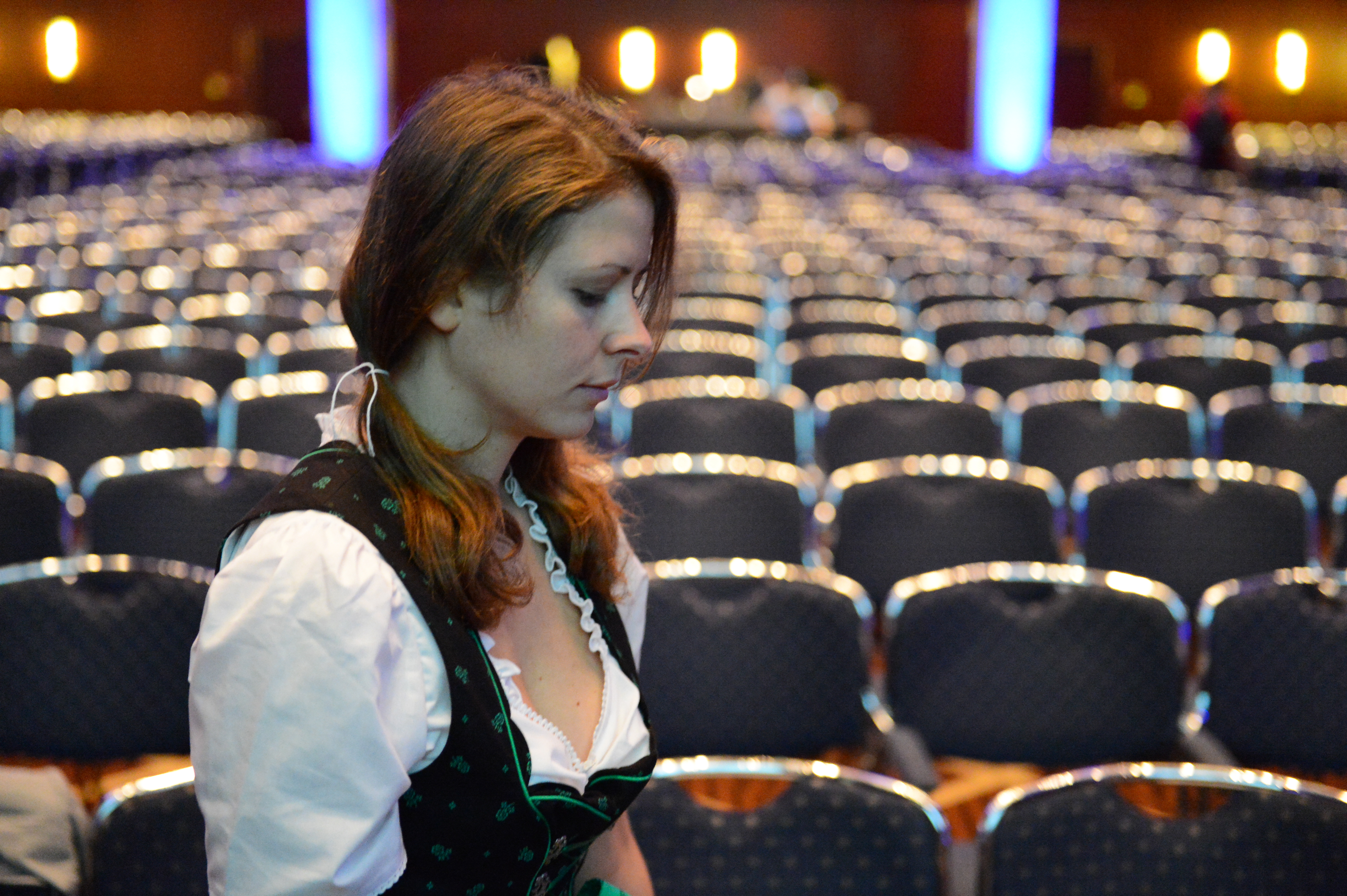 A woman in traditional clothing stands in front of empty conference chairs, looking down thoughtfully.