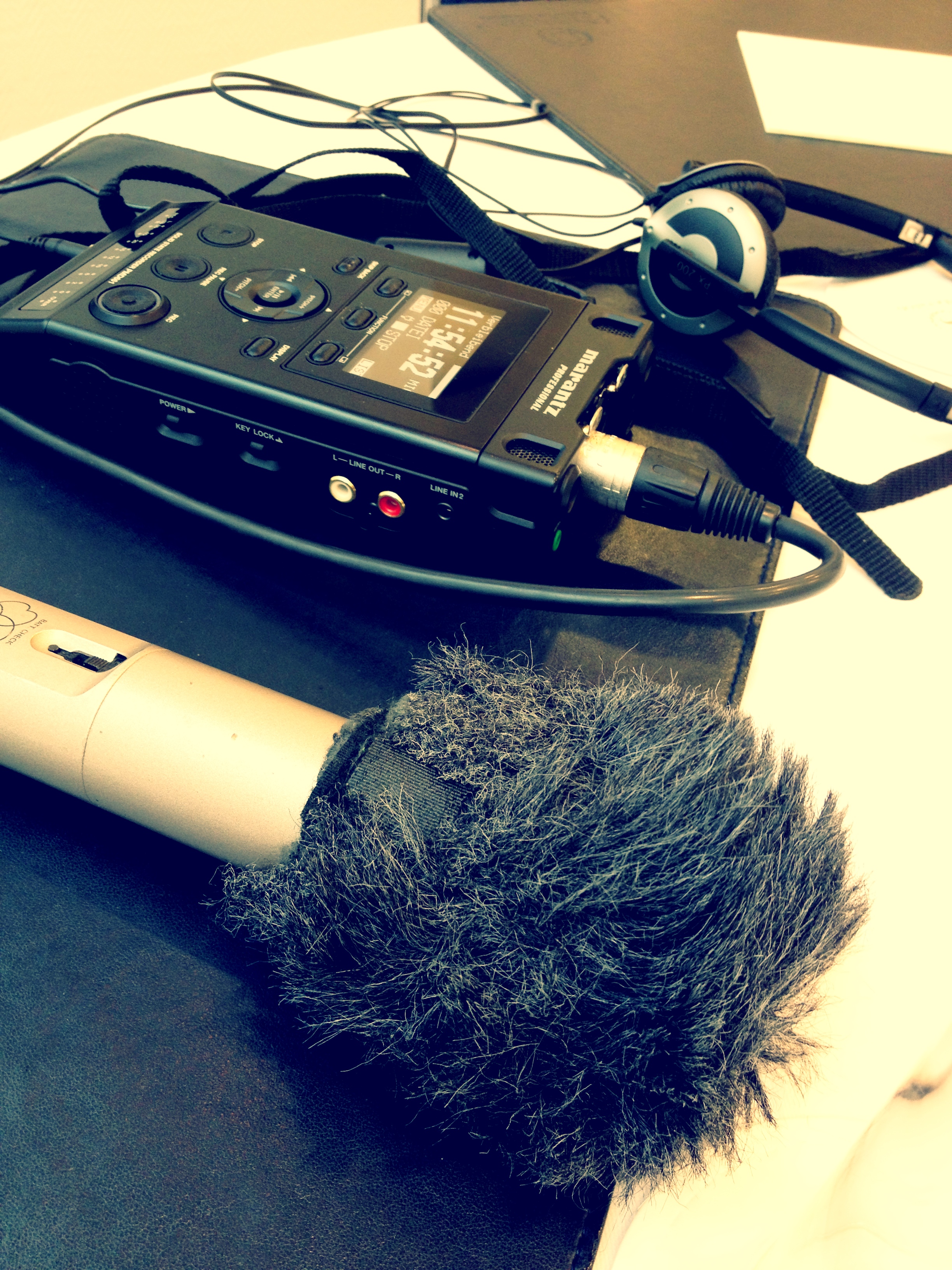 A microphone with a windscreen, an audio recorder, and headphones set up for a radio interview.