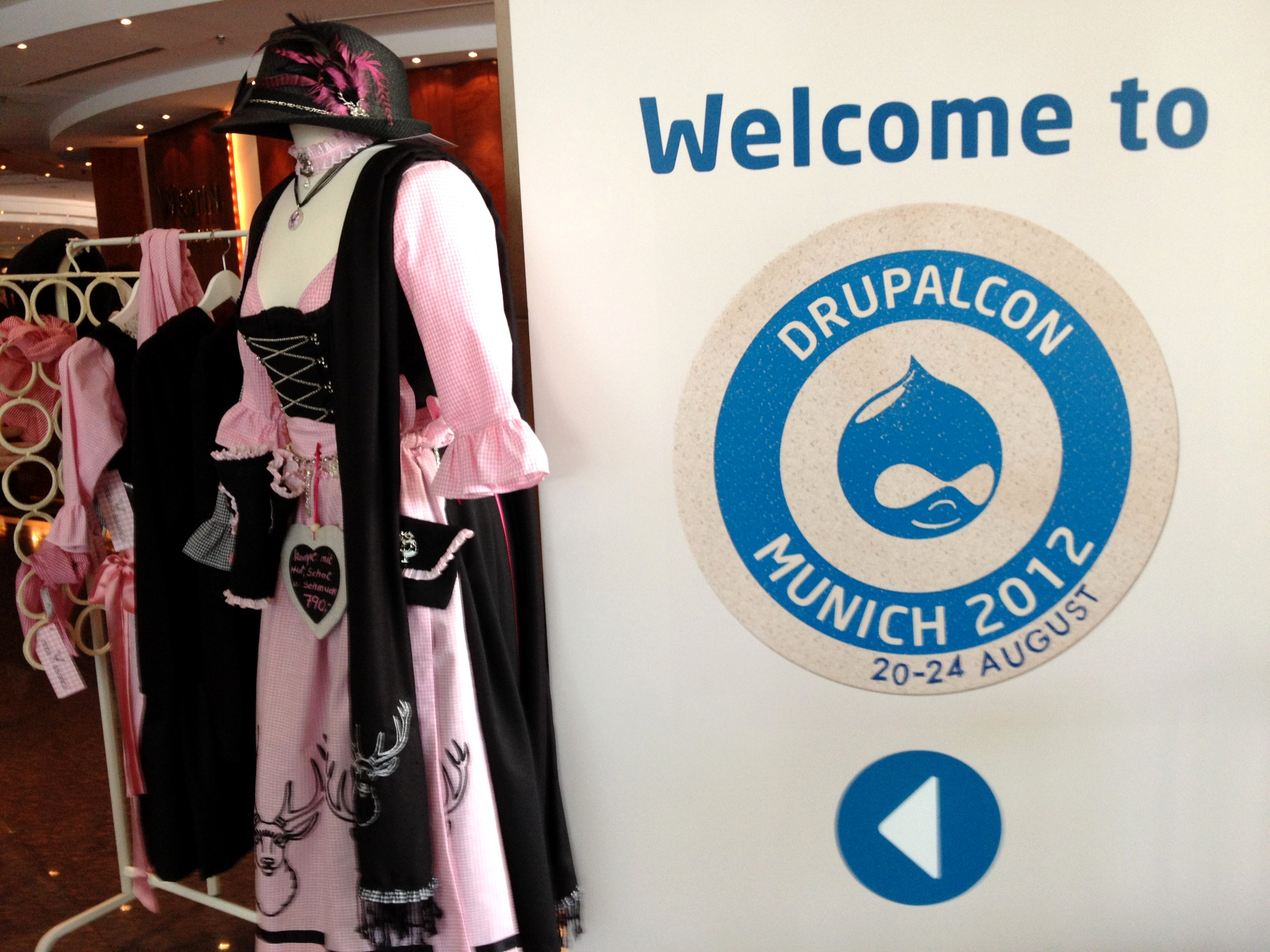 A "Welcome to DrupalCon Munich 2012" sign next to a mannequin dressed in traditional Bavarian clothing.