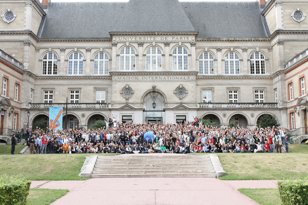 A large group of people gathers outside a historic building for DrupalCon Paris 2009, posing for a group photo.
