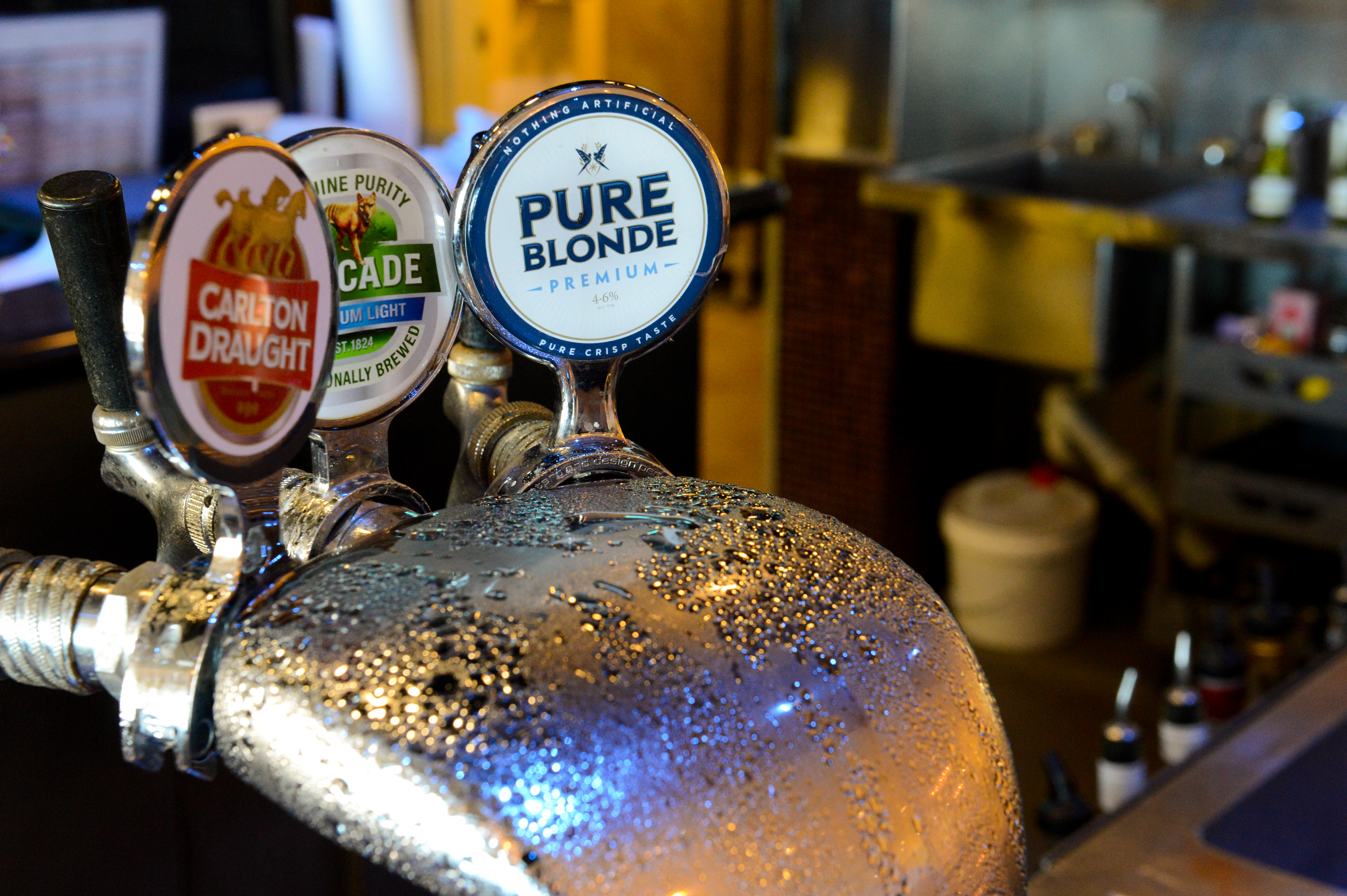 Close-up of beer taps with condensation, featuring Carlton Draught, Cascade, and Pure Blonde labels in a bar setting.
