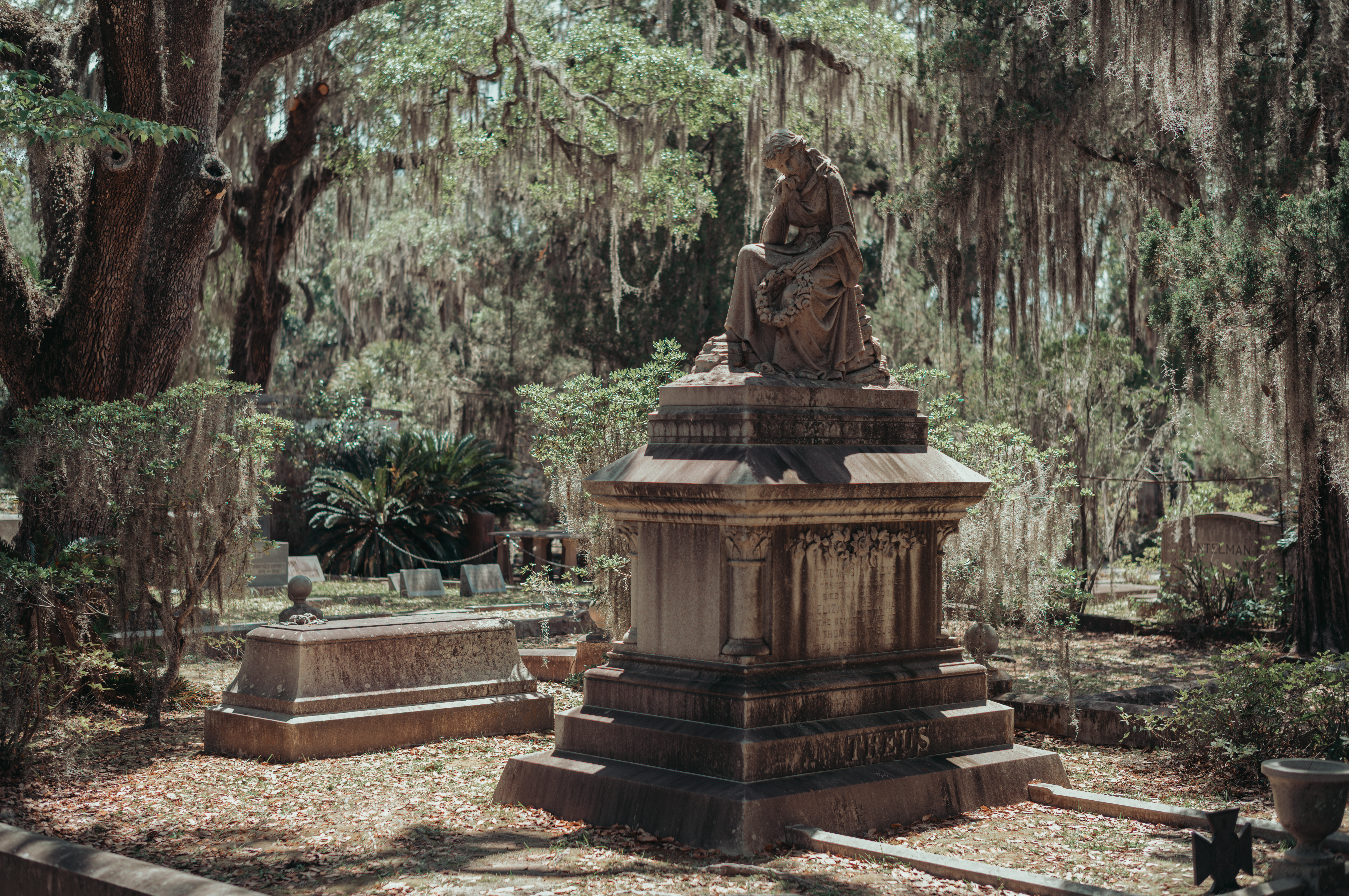 Stone monument beneath live oaks covered in Spanish moss at a cemetery.