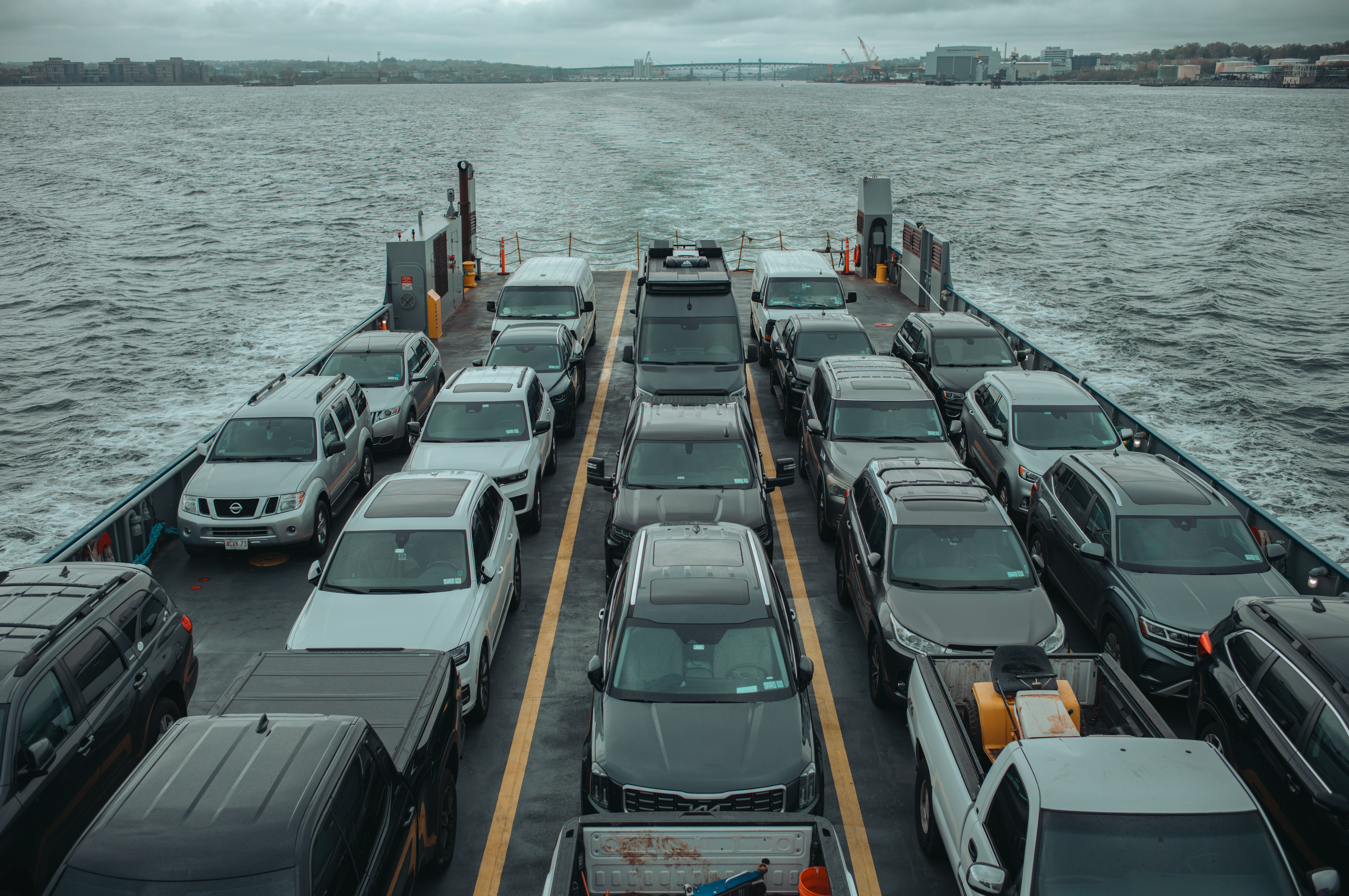 View from the back of a ferry packed with cars and vans crossing open water.