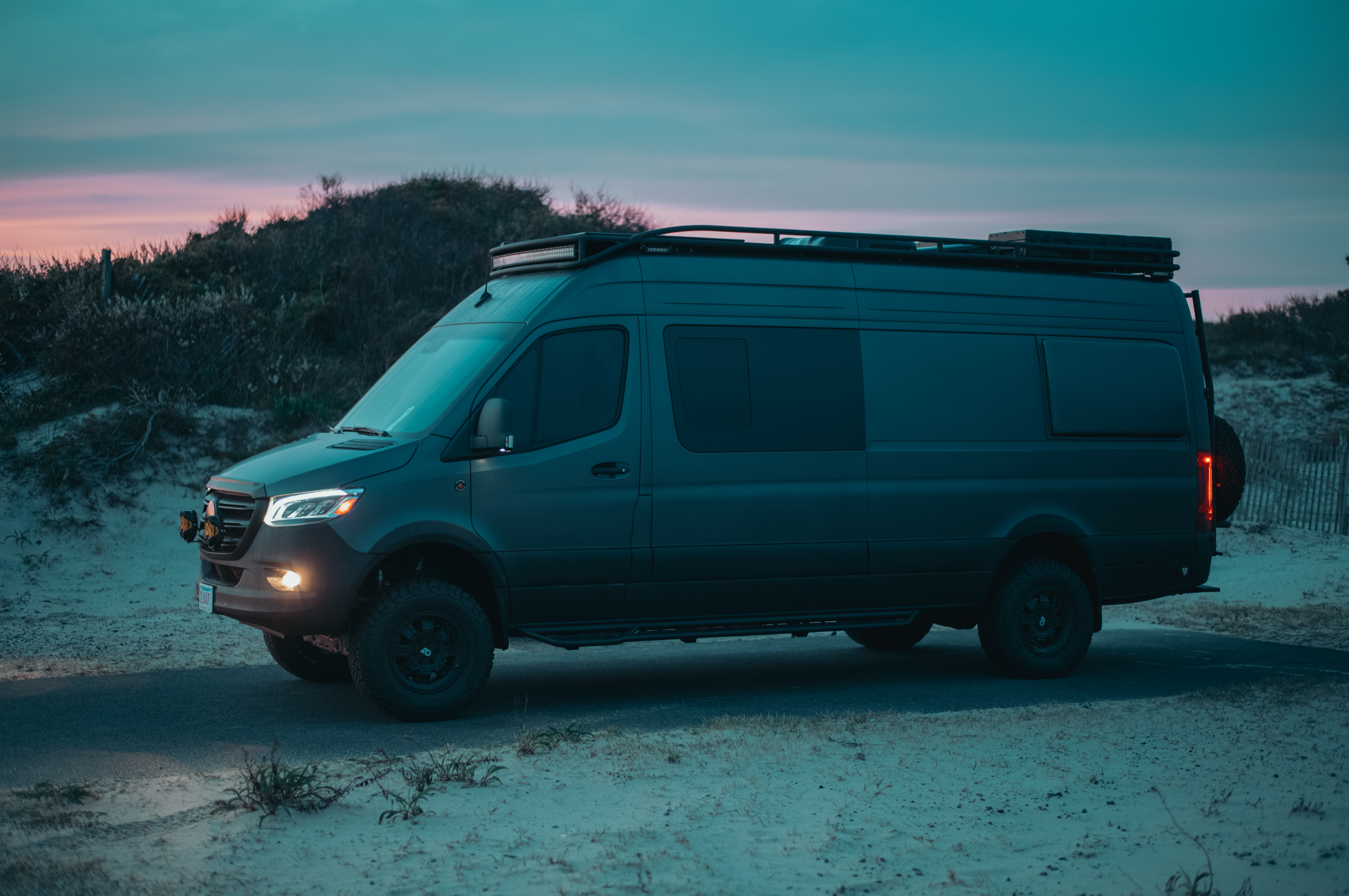 Matte black camper van parked in the dunes during blue hour.