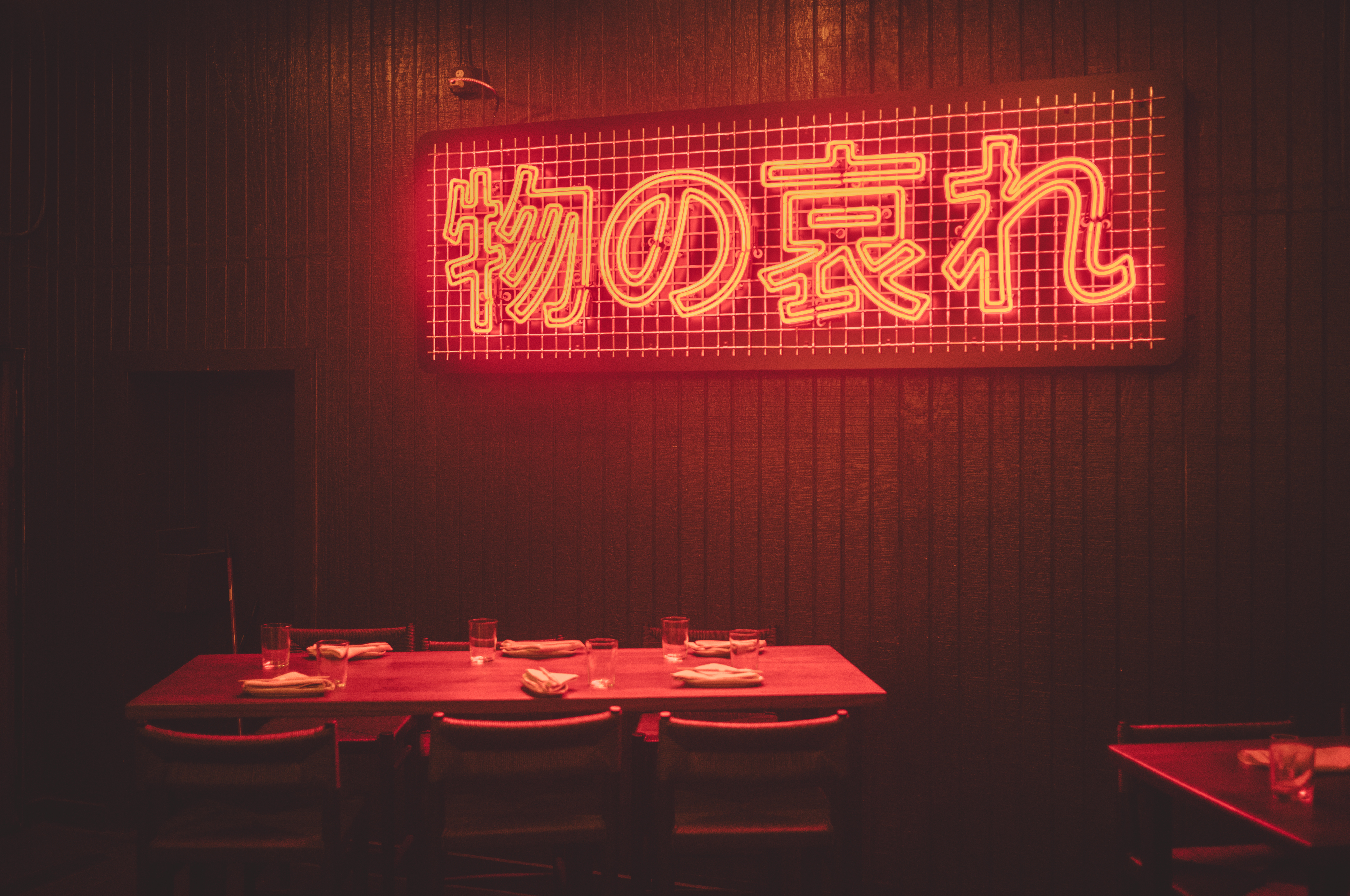 A red neon sign reading 'Mono no aware' on a dark wood wall above an empty restaurant table.