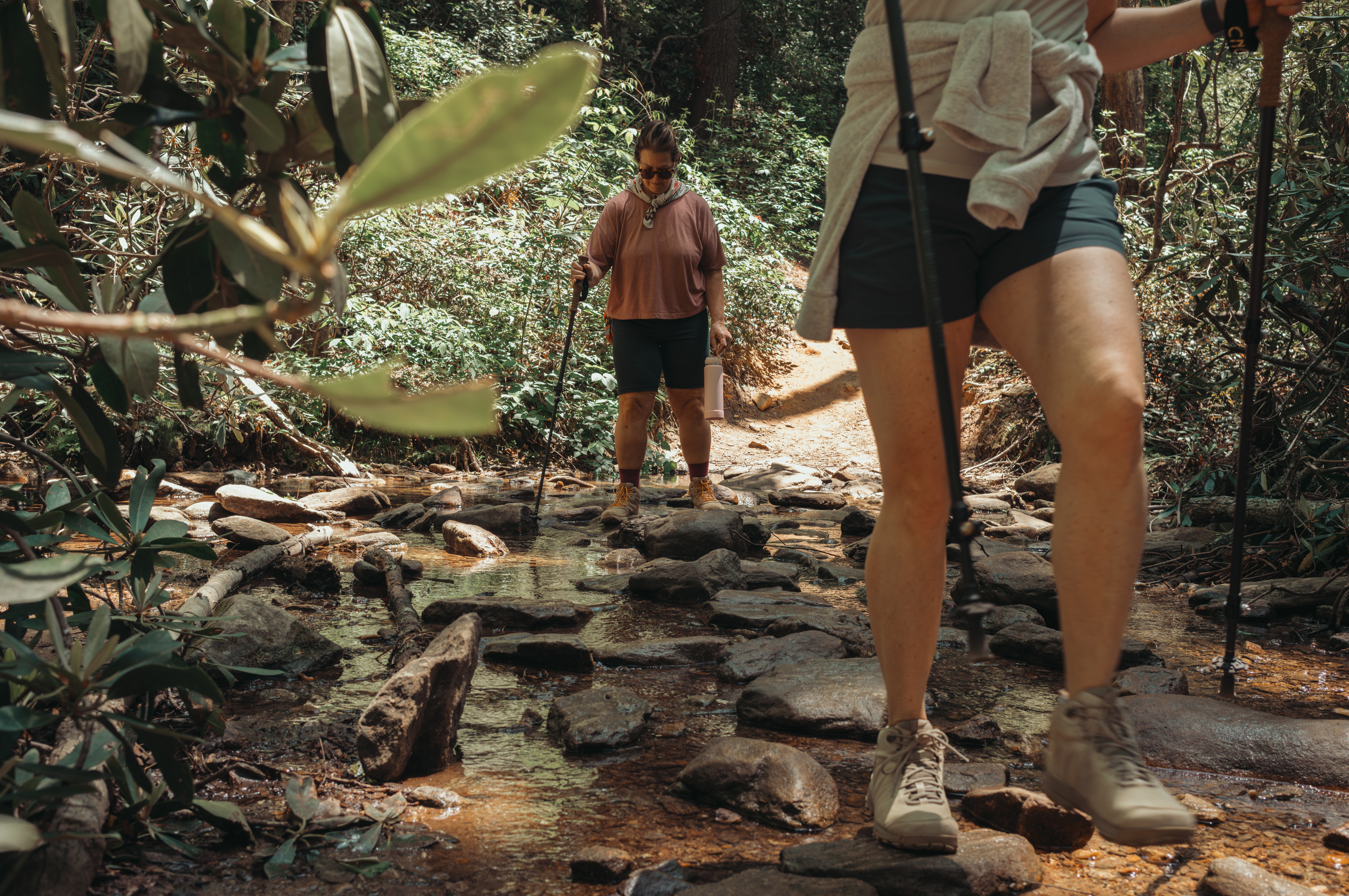 Two hikers with trekking poles crossing a rocky creek.