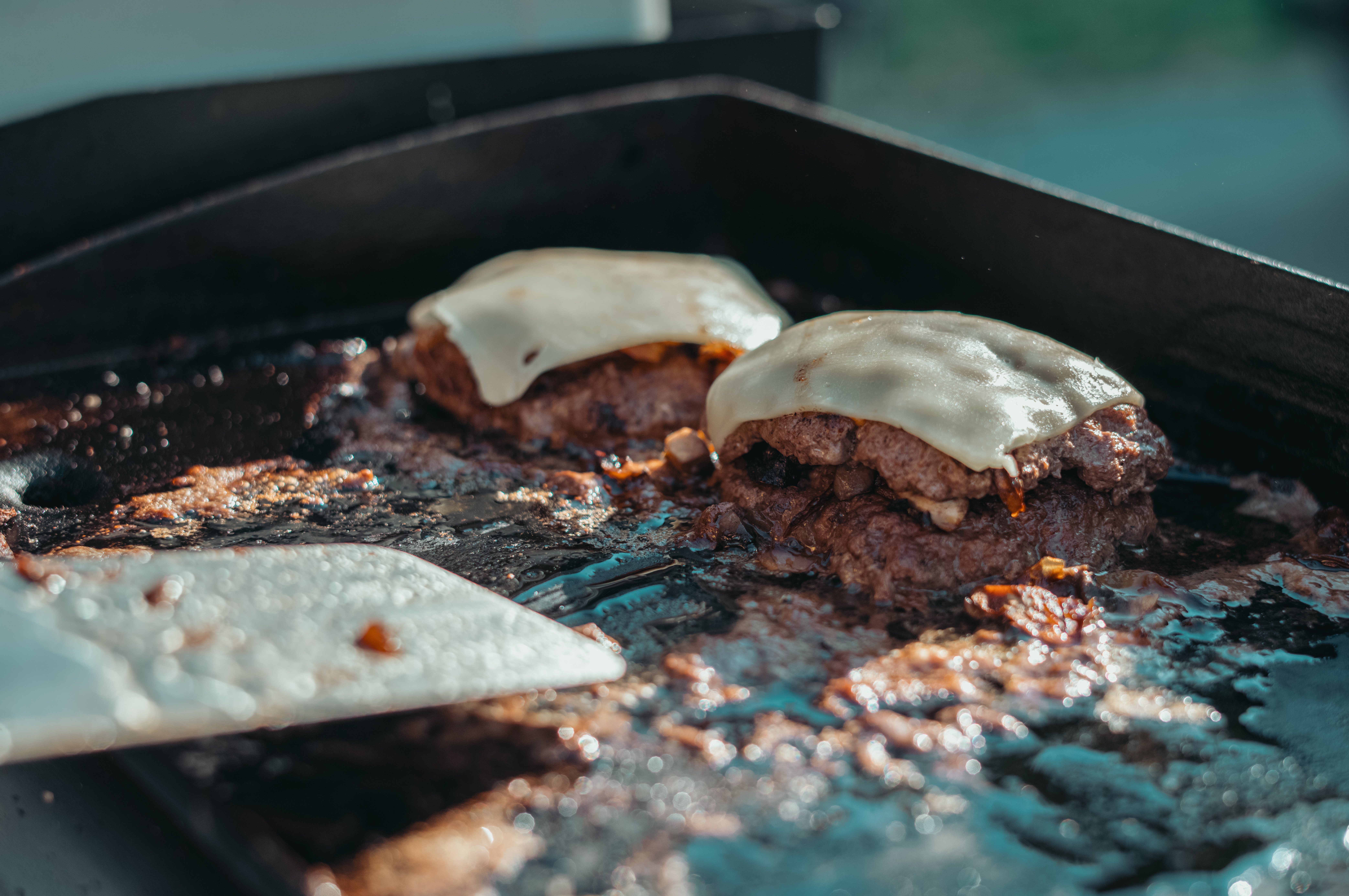 Melted cheese burgers cooking on a cast-iron griddle at a campsite.