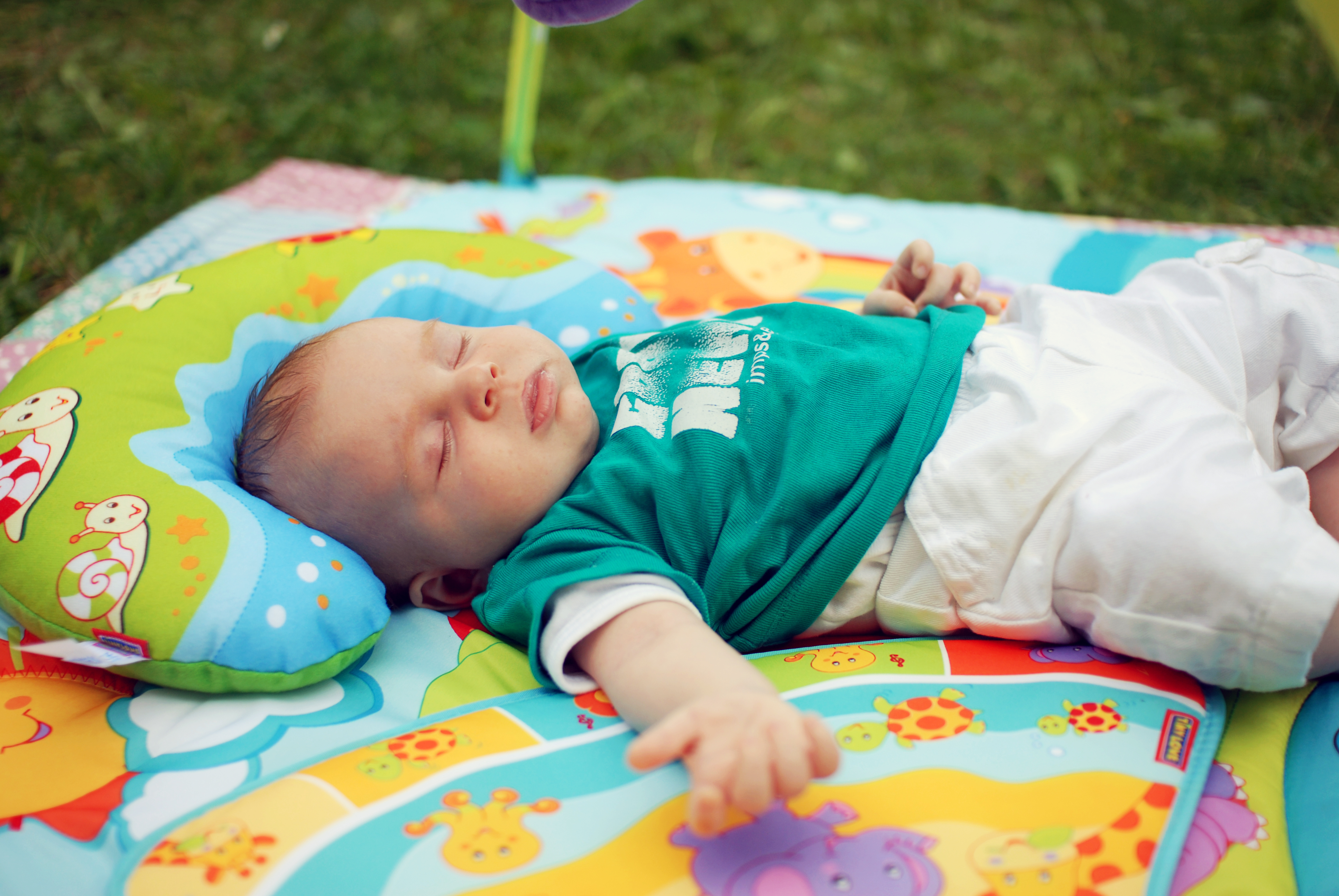 A baby named Stan, 8-9 weeks old, sleeps on a colorful play mat outdoors.