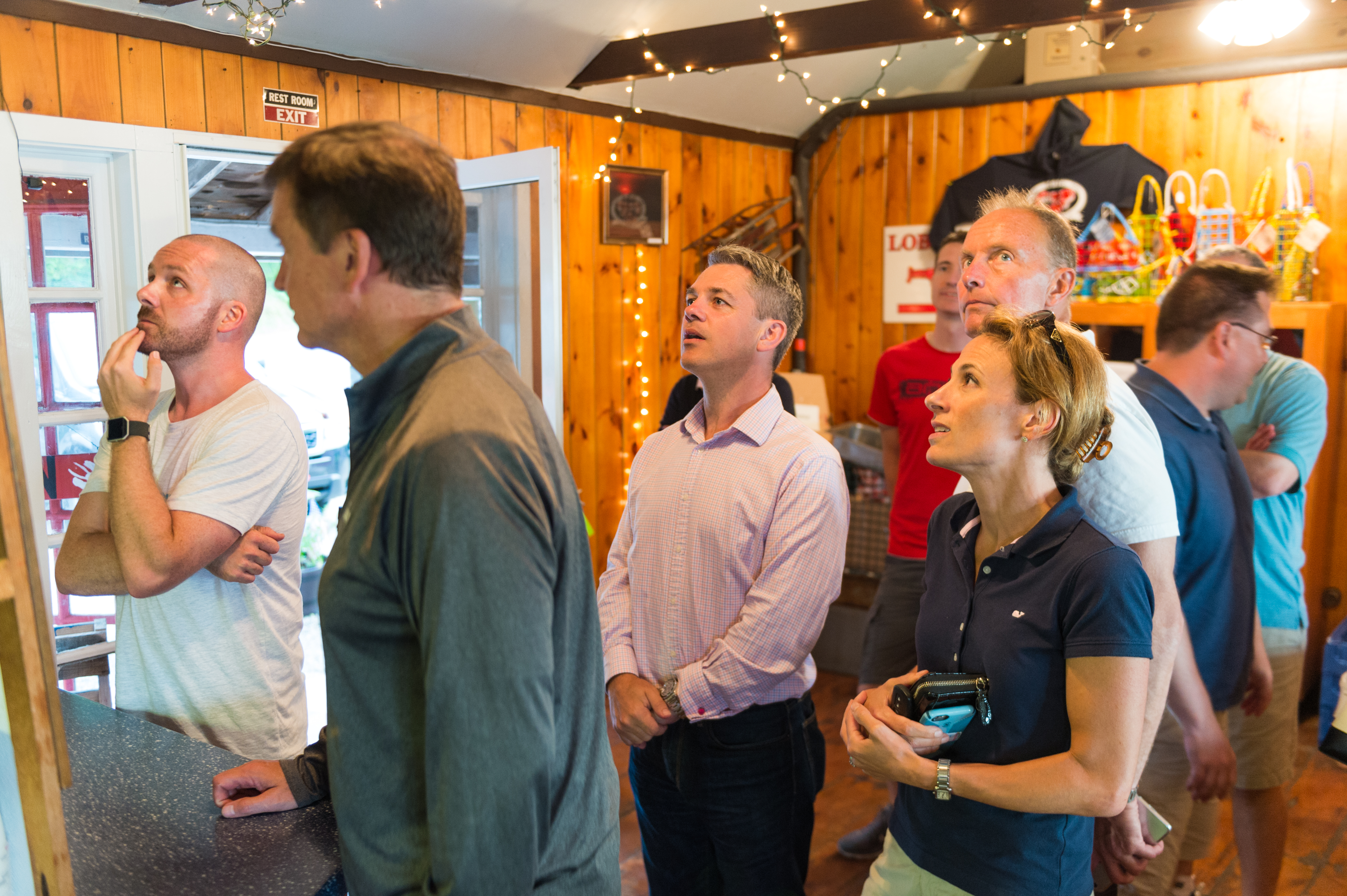 A group of people looks at a menu or board inside a restaurant, deciding on their lobster dinner.