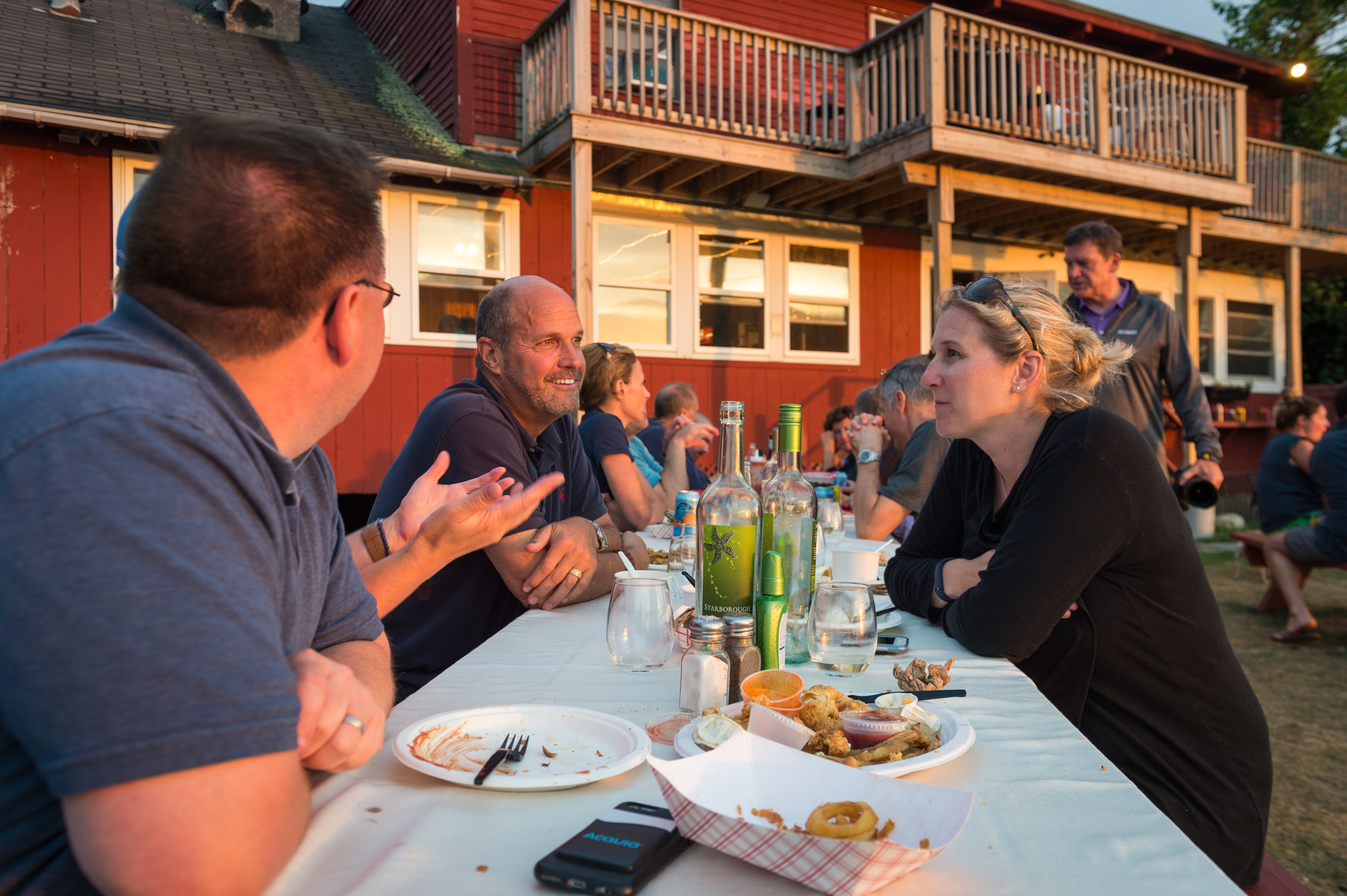 People sitting at an outdoor table, eating and talking during a dinner gathering with seafood and drinks.