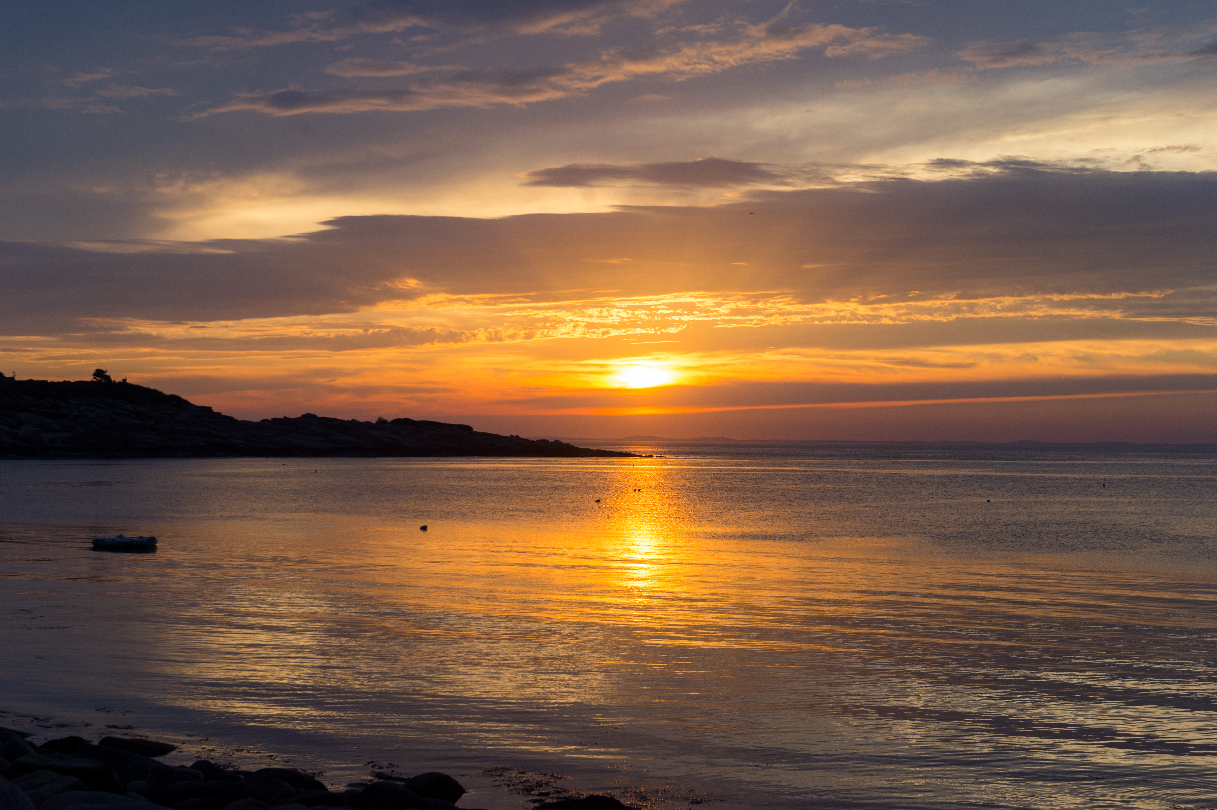 A calm coastal scene at sunset with the sun reflecting on the water.