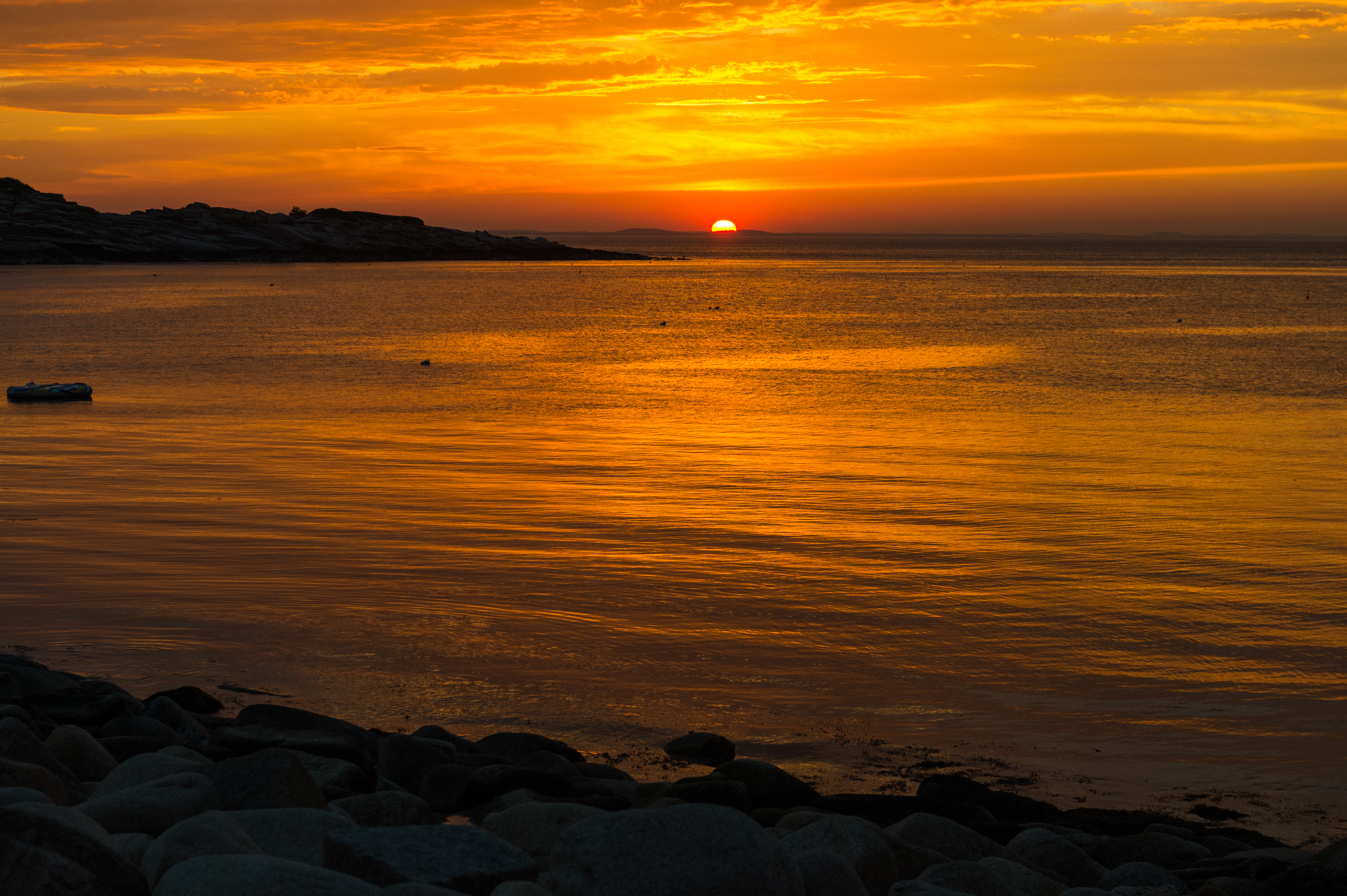 A sunset over the ocean with rocky shoreline in the foreground.