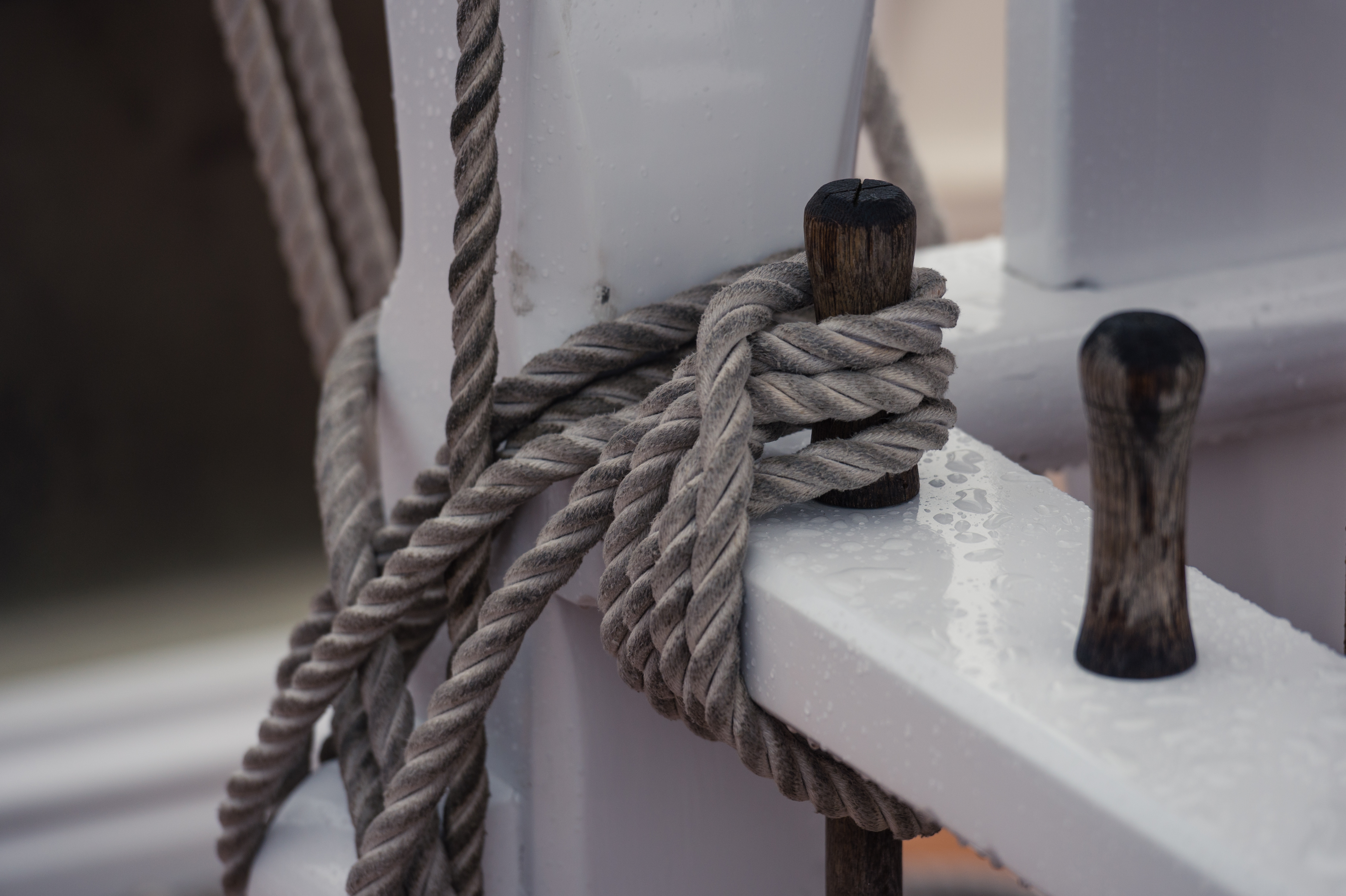 Close-up of a thick rope tightly wrapped around wooden pegs on a wet sailing boat.