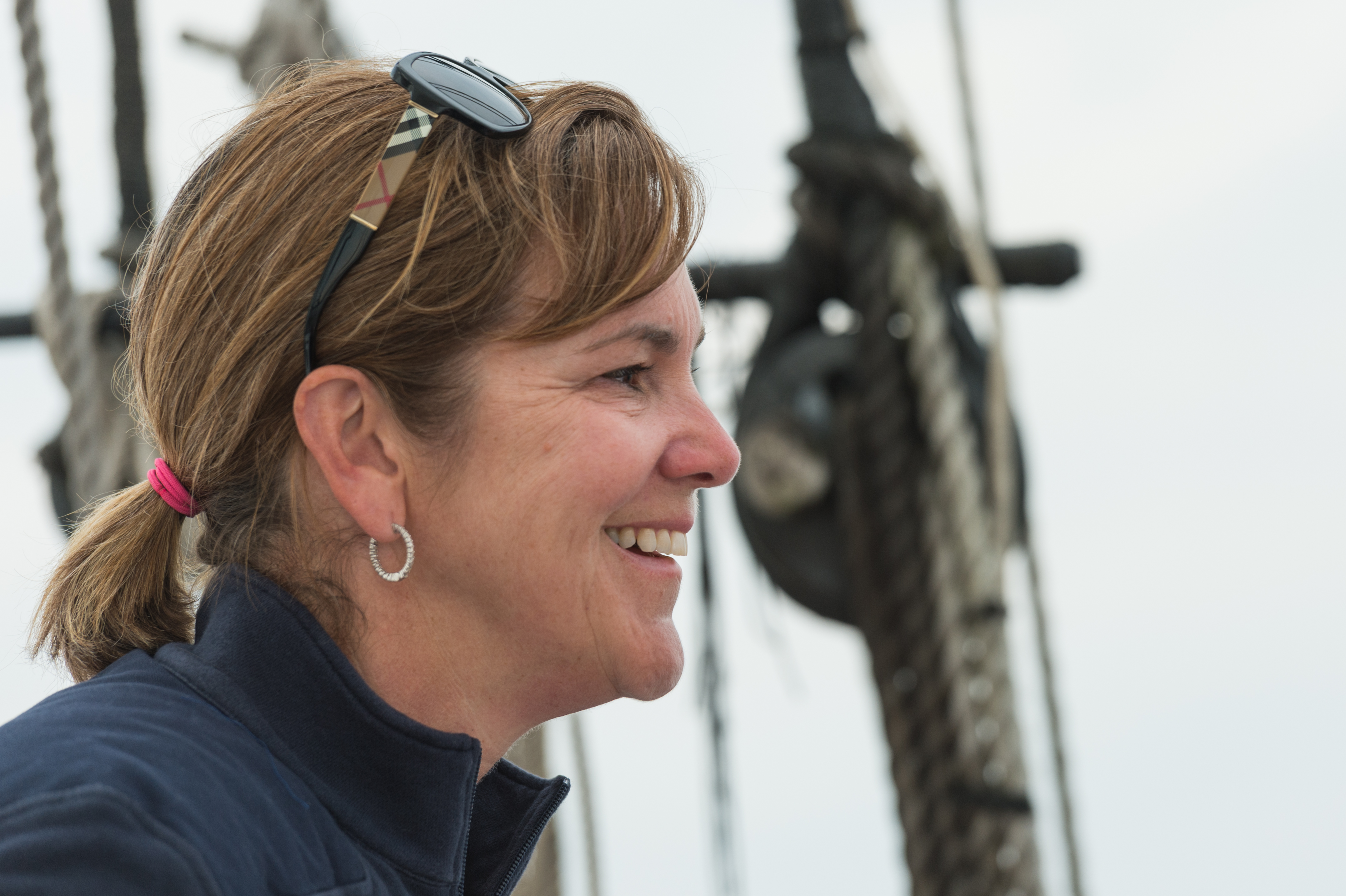 A woman smiles while sailing, with ropes and rigging visible in the background.