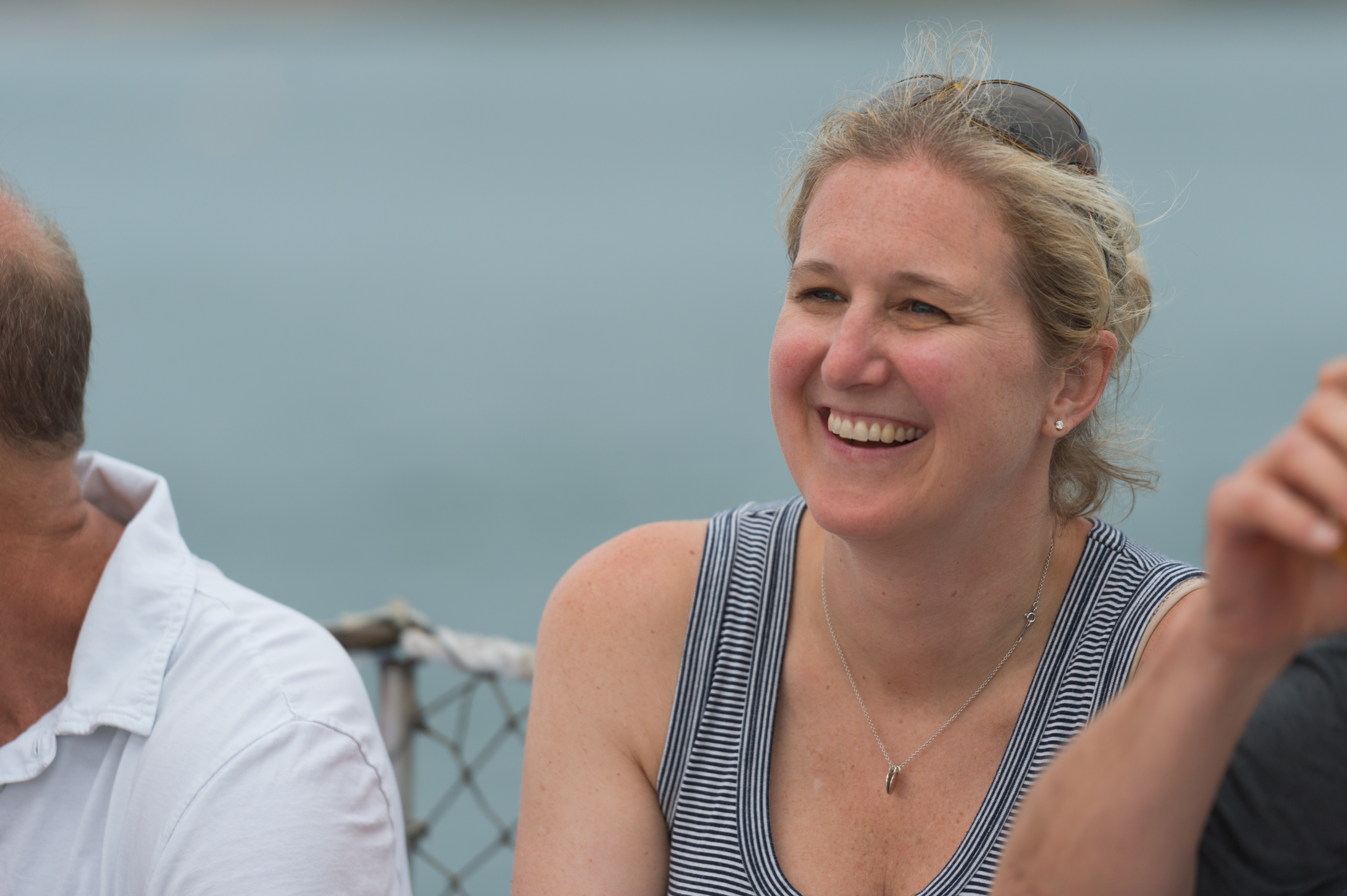 A woman in a striped tank top smiles while sailing with others on a boat.
