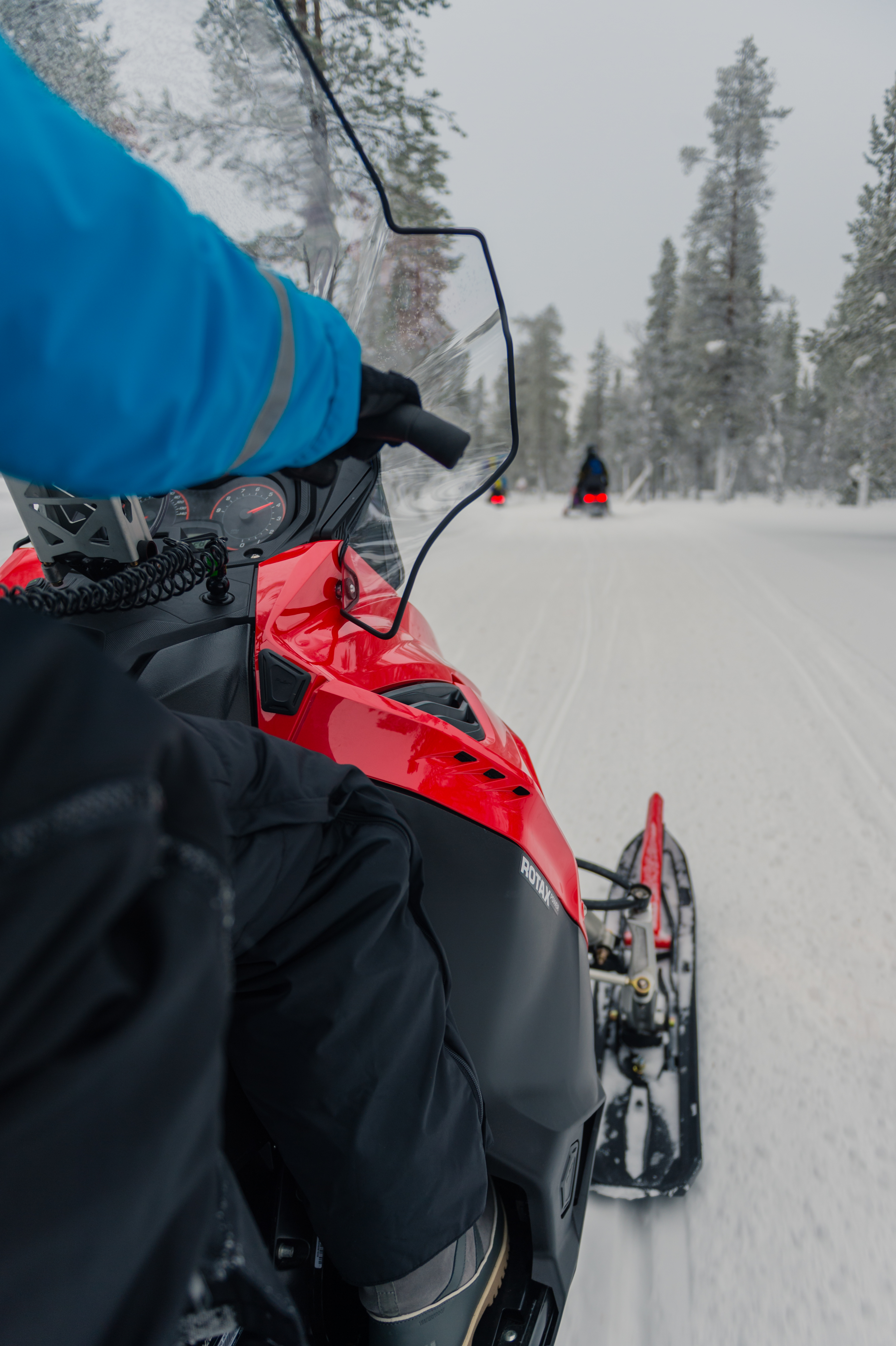 Person riding a red snowmobile on a snowy trail, following others through a winter landscape in Lapland.