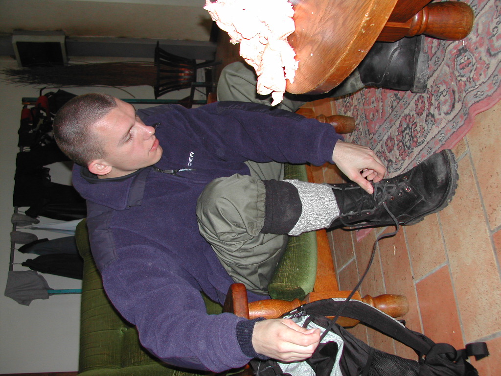 A person sits on a chair, tying the laces of their black boots while preparing for an activity.