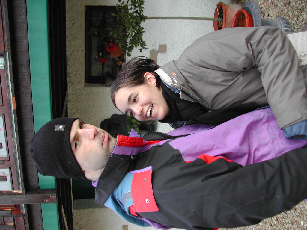 A man in a black beanie looks serious while a woman in a winter jacket smiles and leans toward him.