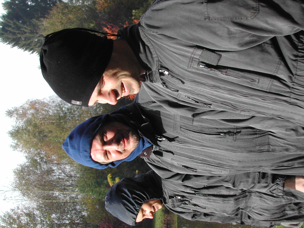 A group of people in matching black jackets and hats stand outdoors, smiling and engaged in conversation.