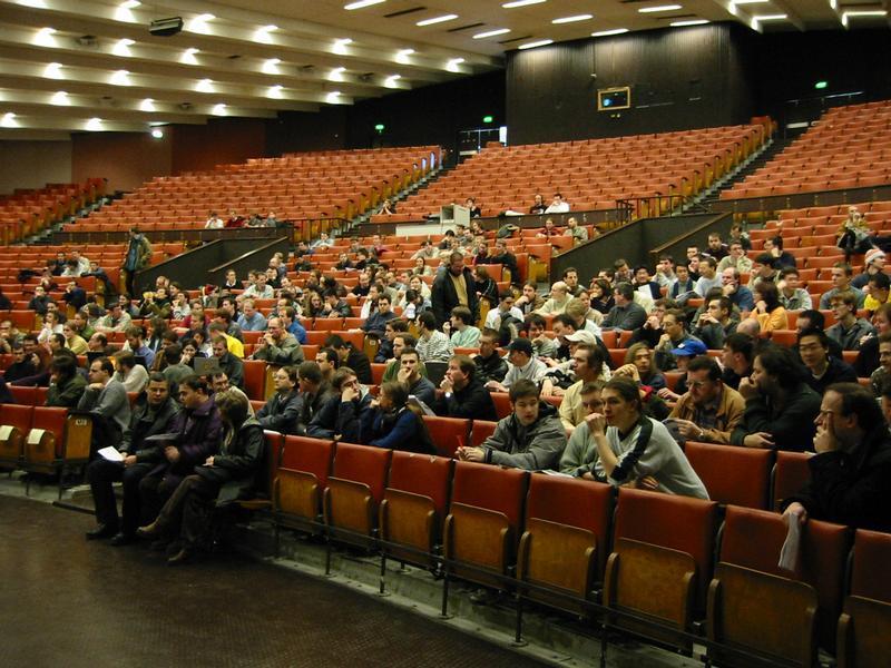 A large audience sits in an auditorium, waiting for a presentation or event to begin.