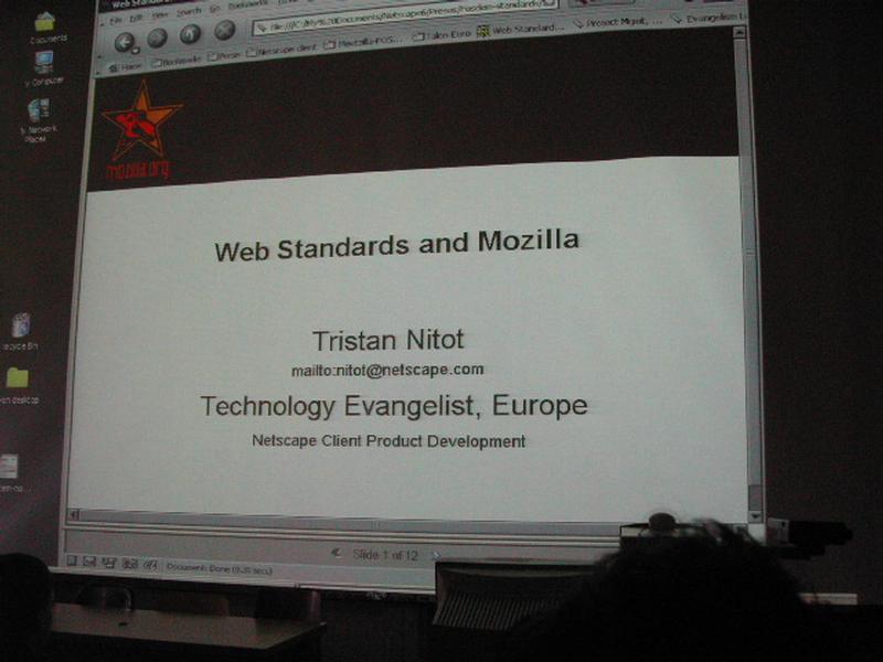 A presentation slide projected on a screen displays "Web Standards and Mozilla" by Tristan Nitot from Netscape.