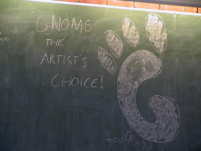 A chalkboard with "GNOME the artist's choice!" written in chalk, alongside a large GNOME logo drawing.