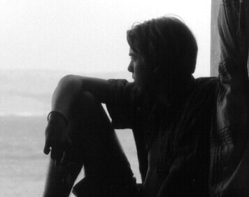 A person sits near a window, looking outside with a relaxed posture.