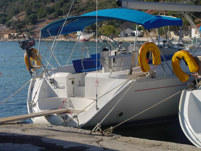 A white sailboat with a blue canopy is docked at a pier, with yellow life rings attached.